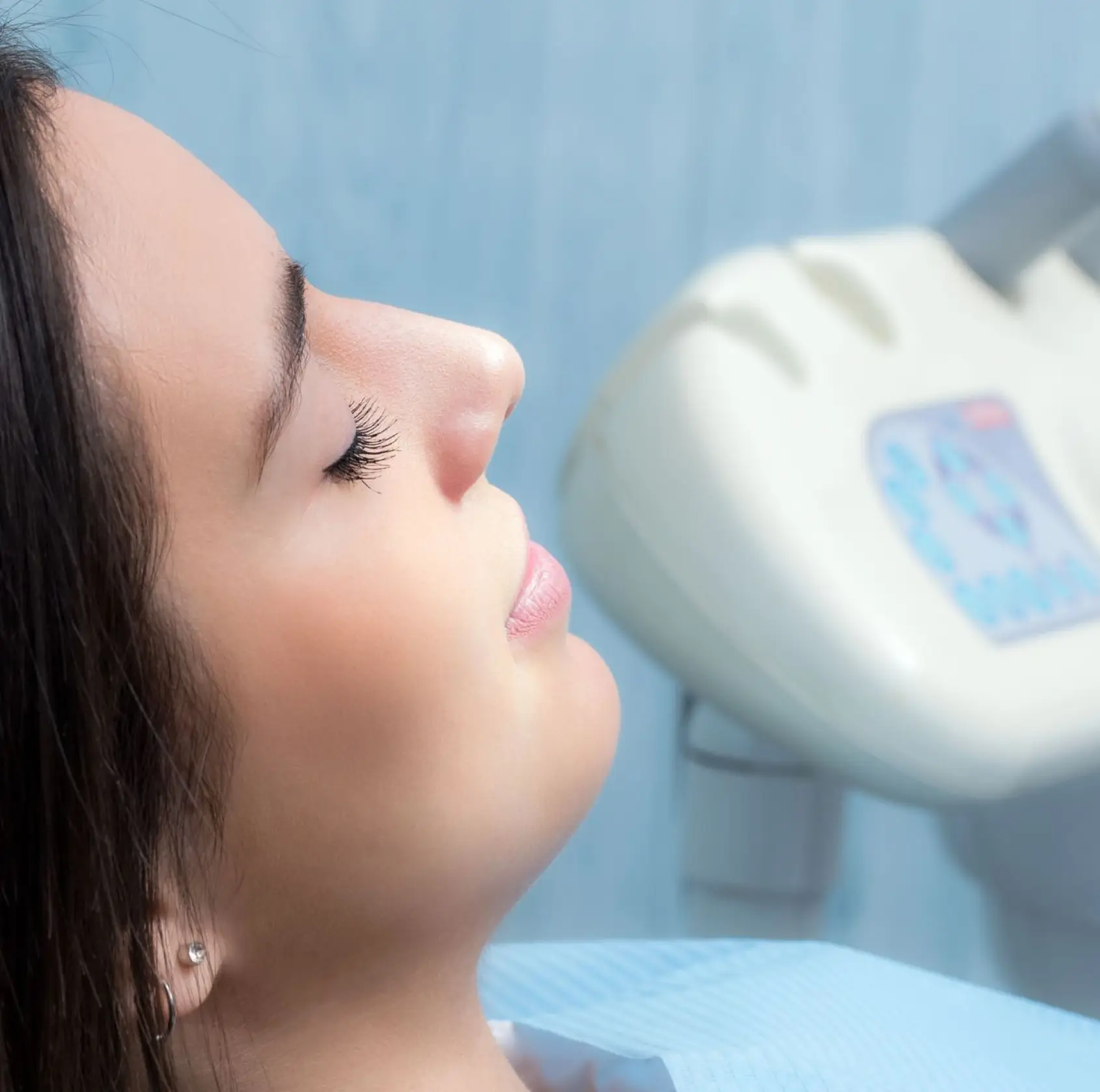 Woman with closed eyes reclining in a dental chair near dental X-ray equipment.
