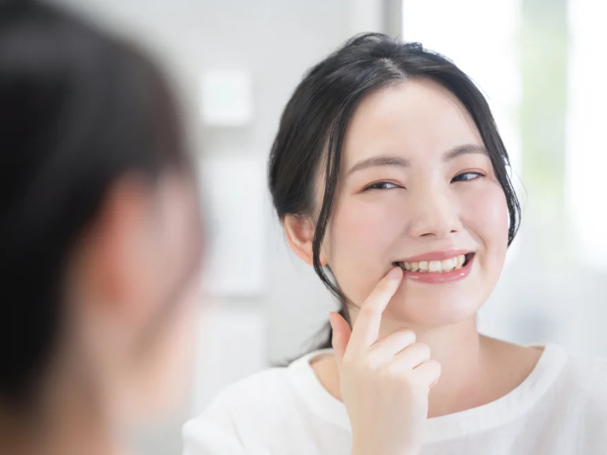 Smiling woman pointing to her teeth while looking in a mirror, showing dental care.