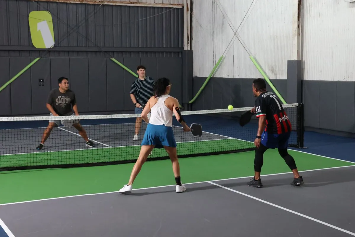 Four players rallying at the net during pickleball open play at NOLA PicklePlex