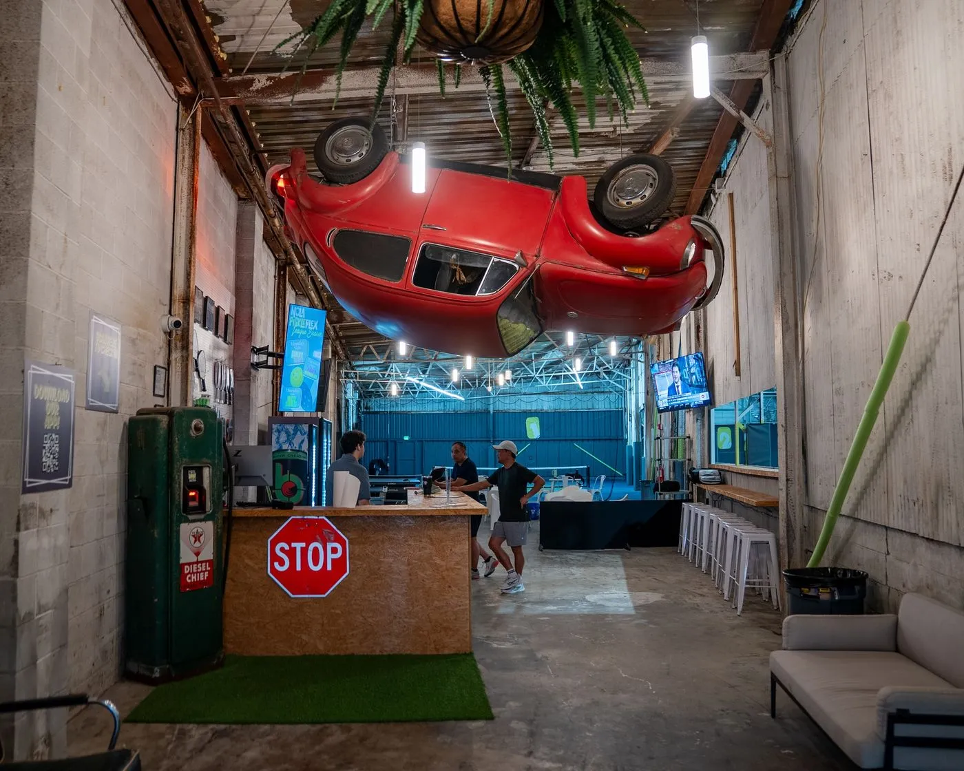 Lounge and bar at NOLA PicklePlex with a red car hanging upside down from the ceiling