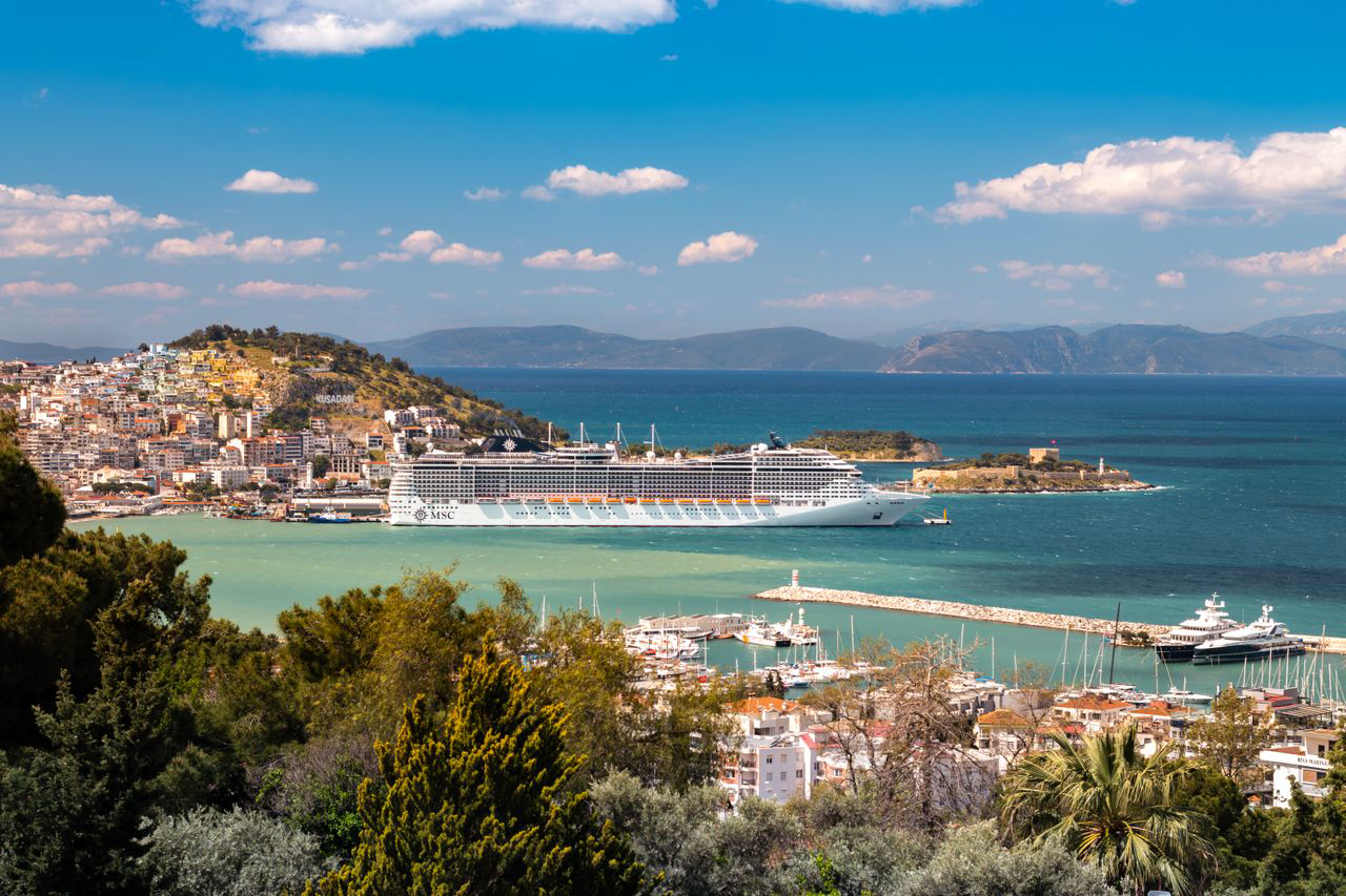 A cruise ship docked in a sunlit Mediterranean harbor