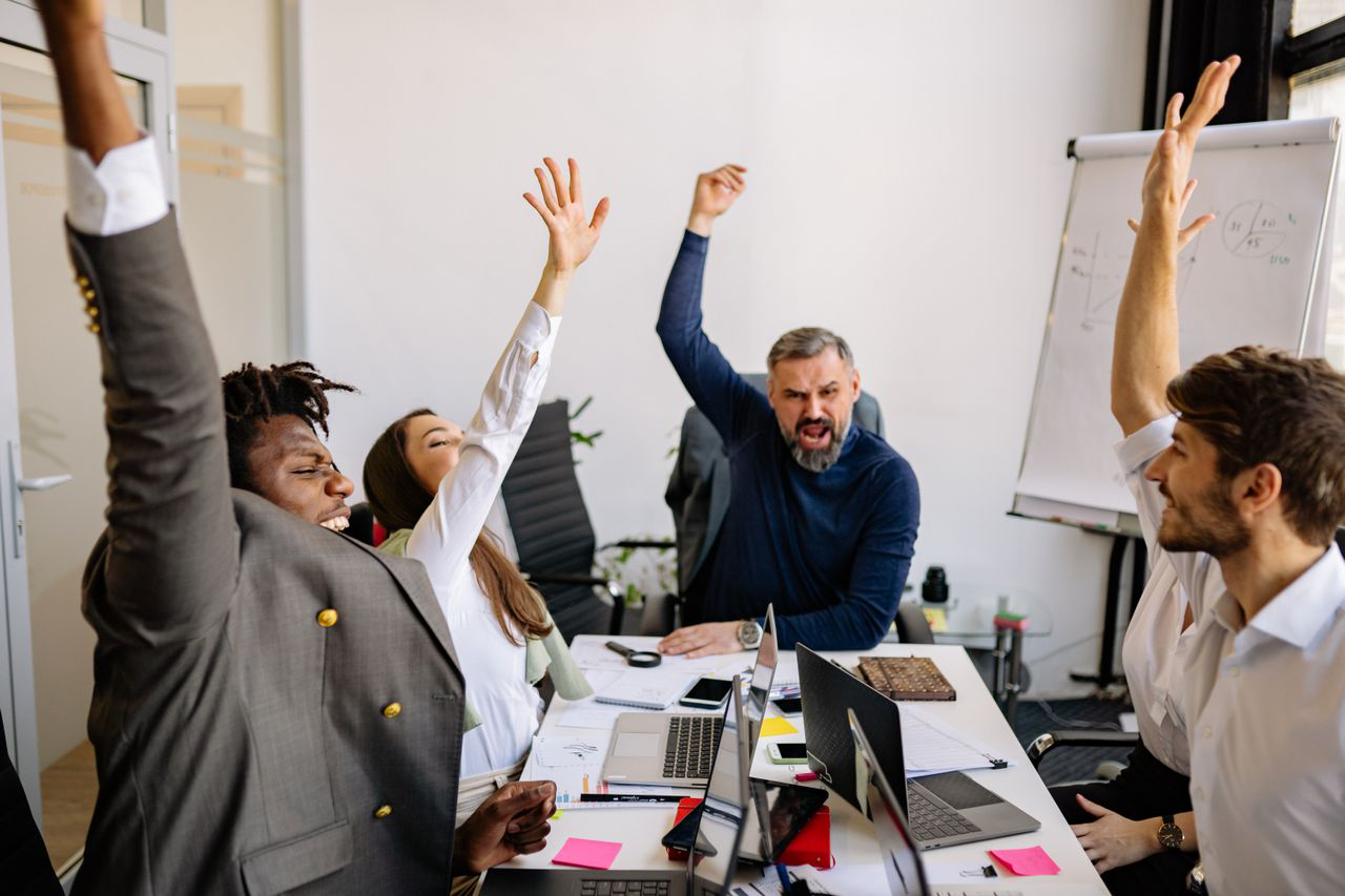 A team in an office cheering with their arms raised