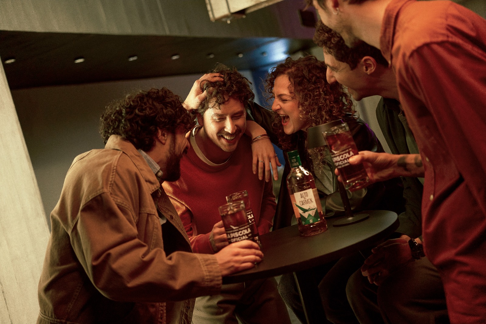 Grupo de amigos riendo alrededor de una mesa con piscolas y una botella de Alto del Carmen Especial