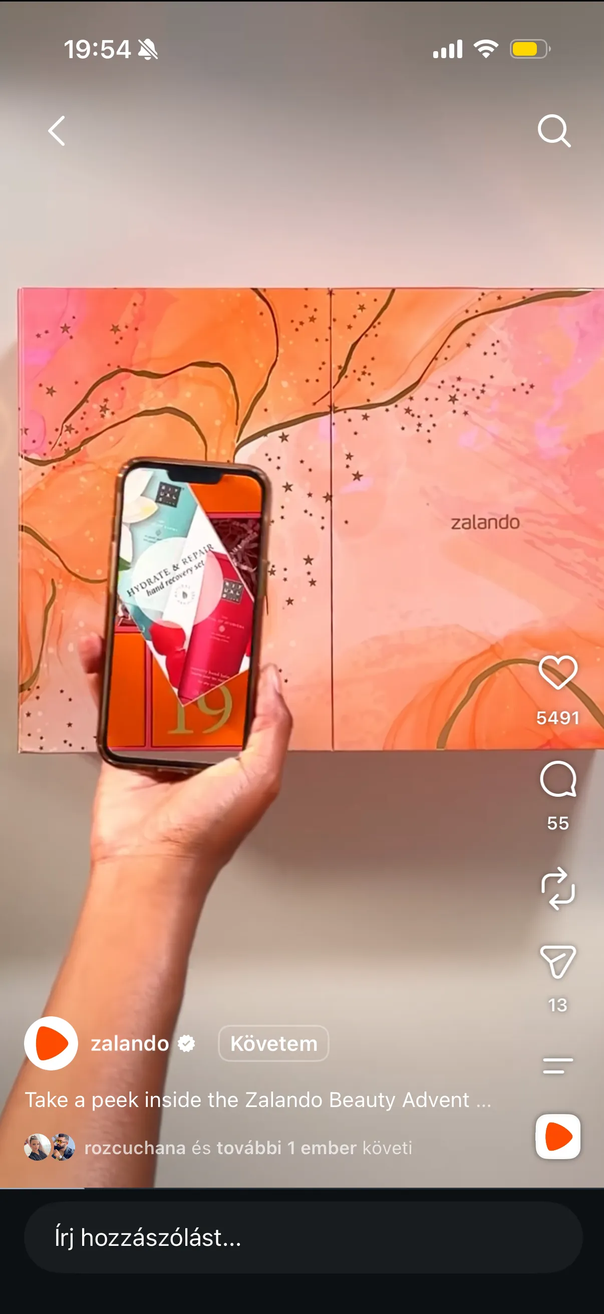 A hand holding a phone with a festive illustration, against a patterned wall
