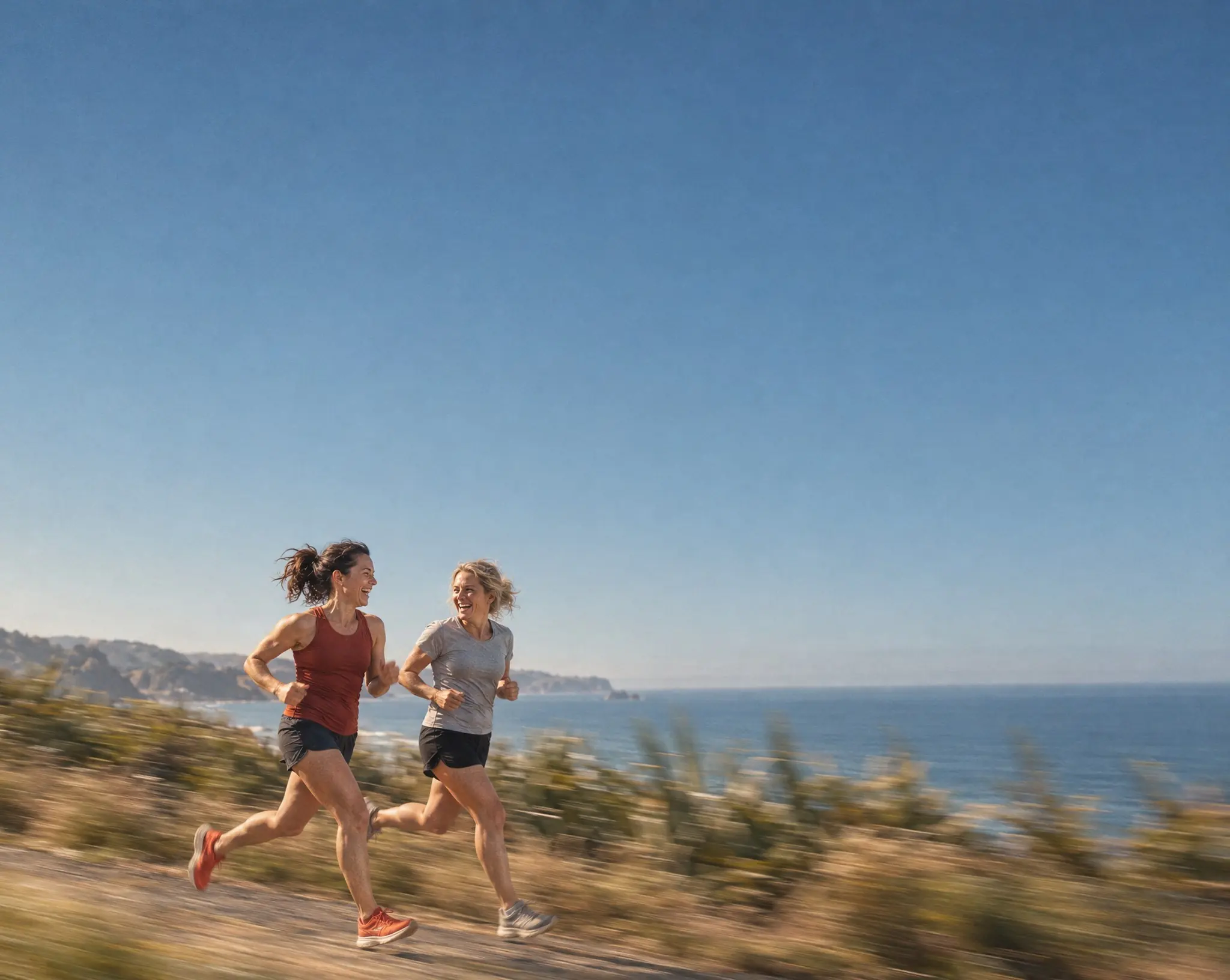 Two women running and laughing on a coastal path