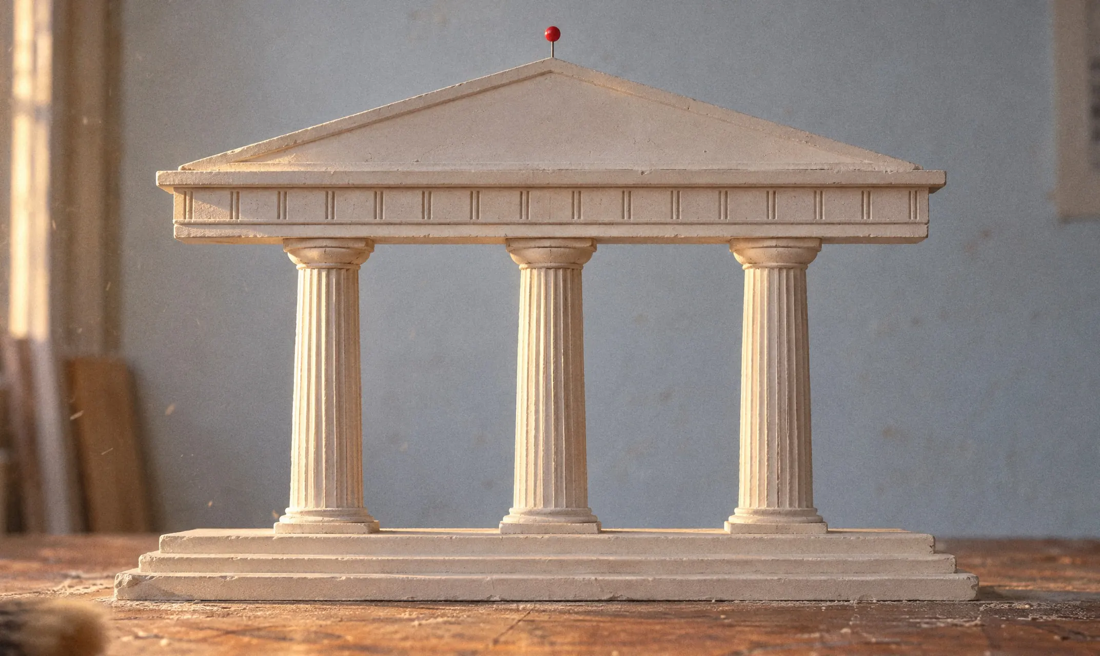 A plaster model of a classical temple with three columns on a workbench