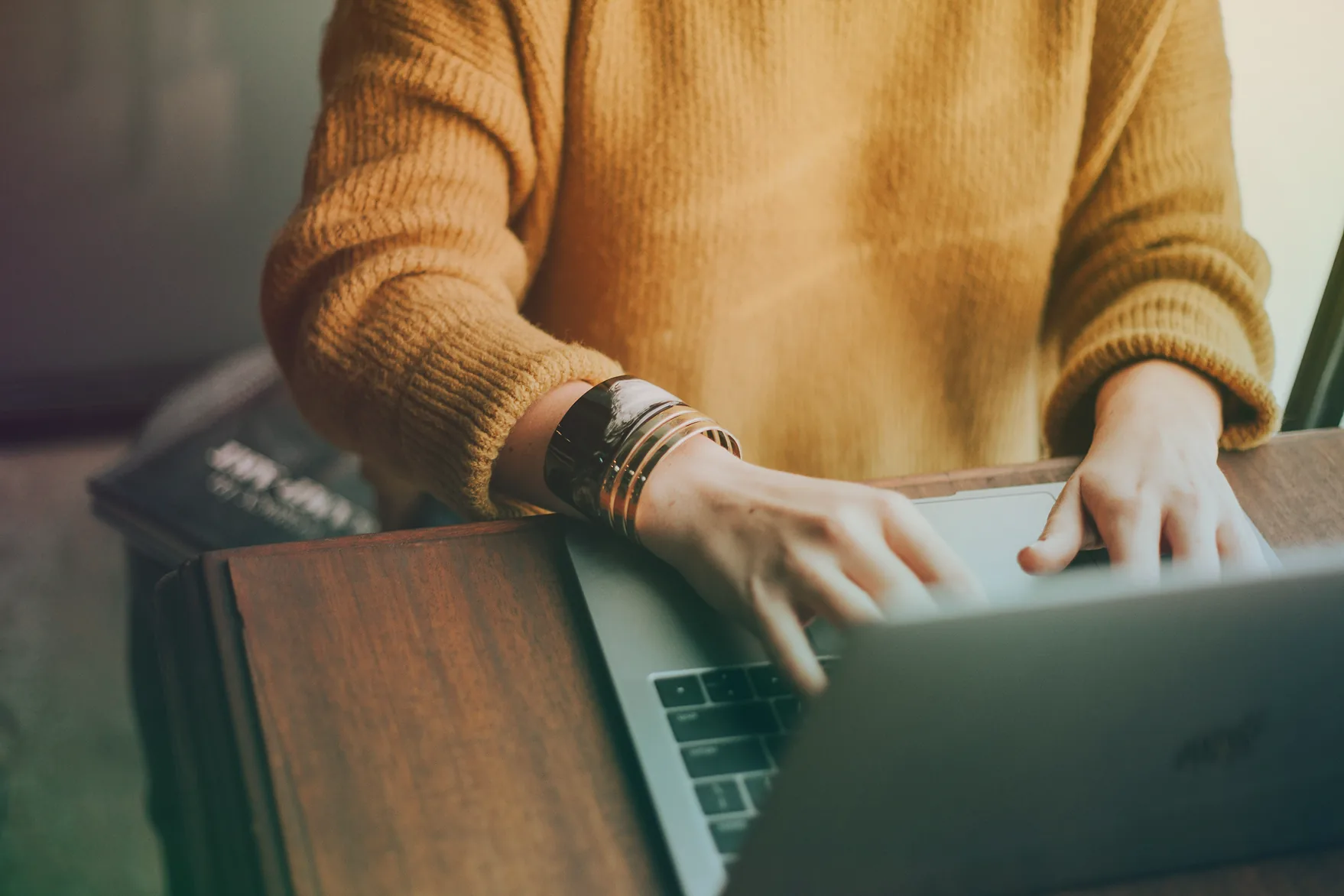 A person typing on a laptop at a wooden table
