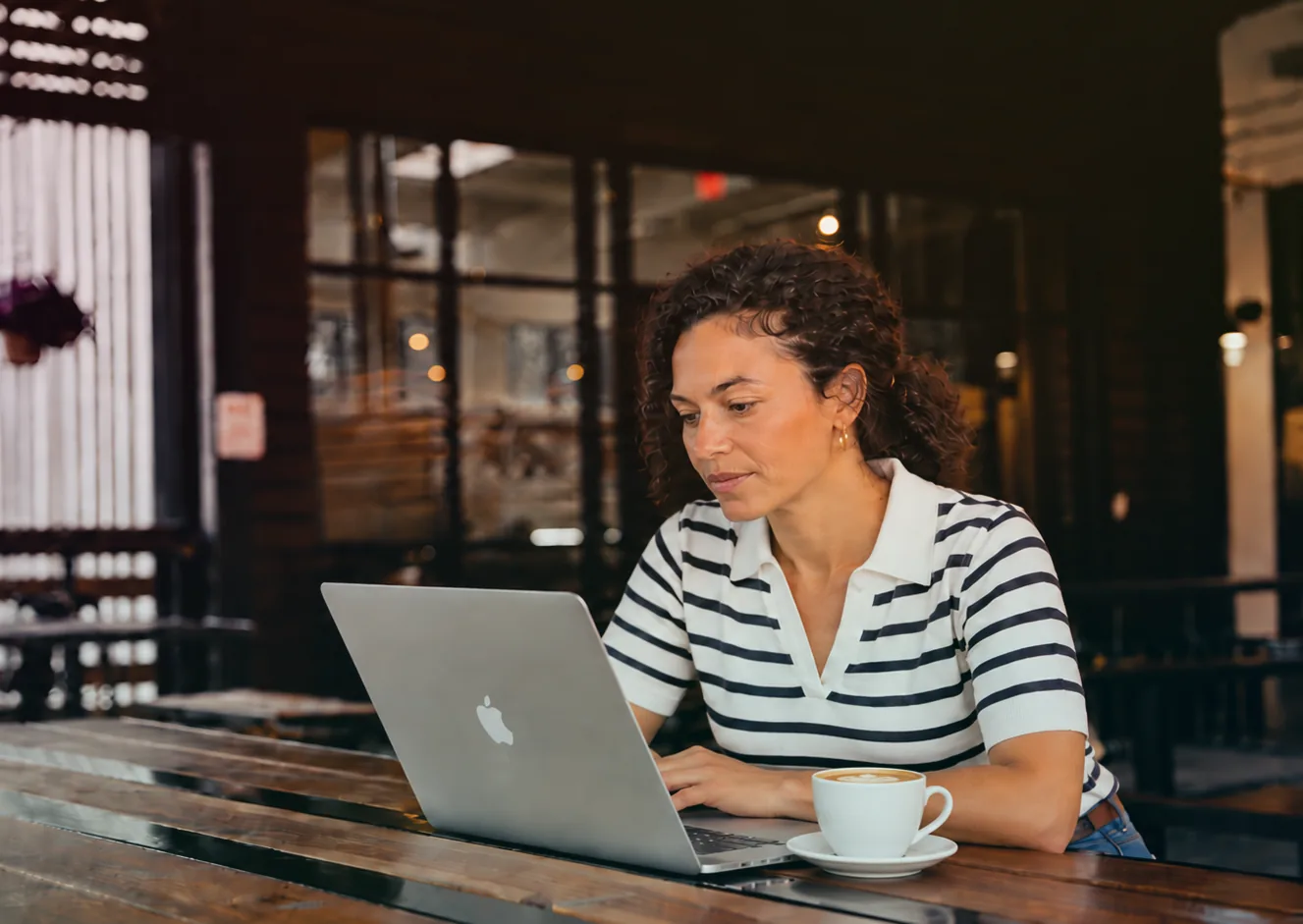 A person at a café table working through paperwork on a laptop