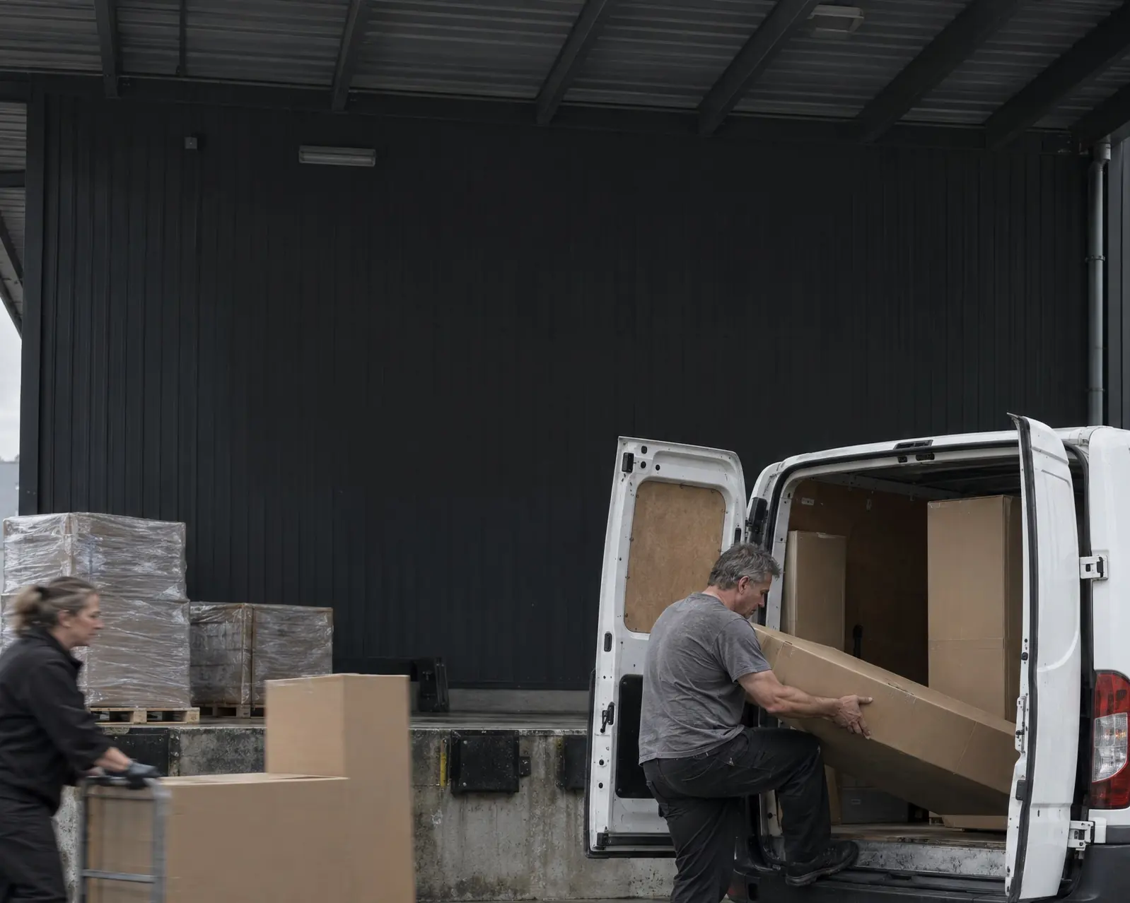 Two people loading boxes into a van at a warehouse dock