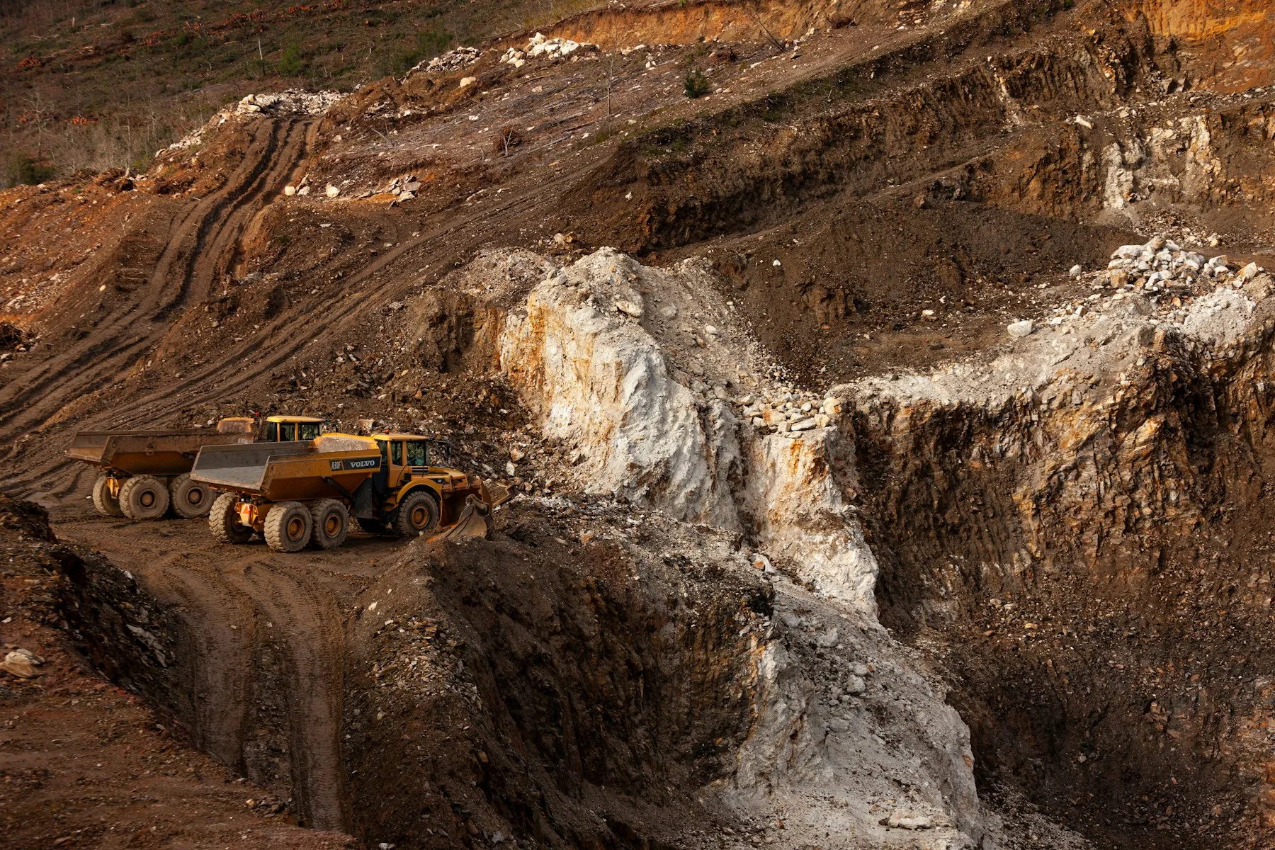 Haul trucks travelling on a terraced road through an open-pit mine.