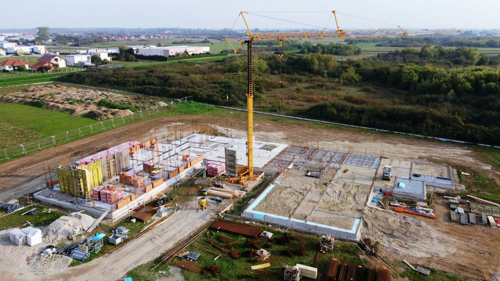 Aerial view of a large building site with a tower crane and concrete structures.