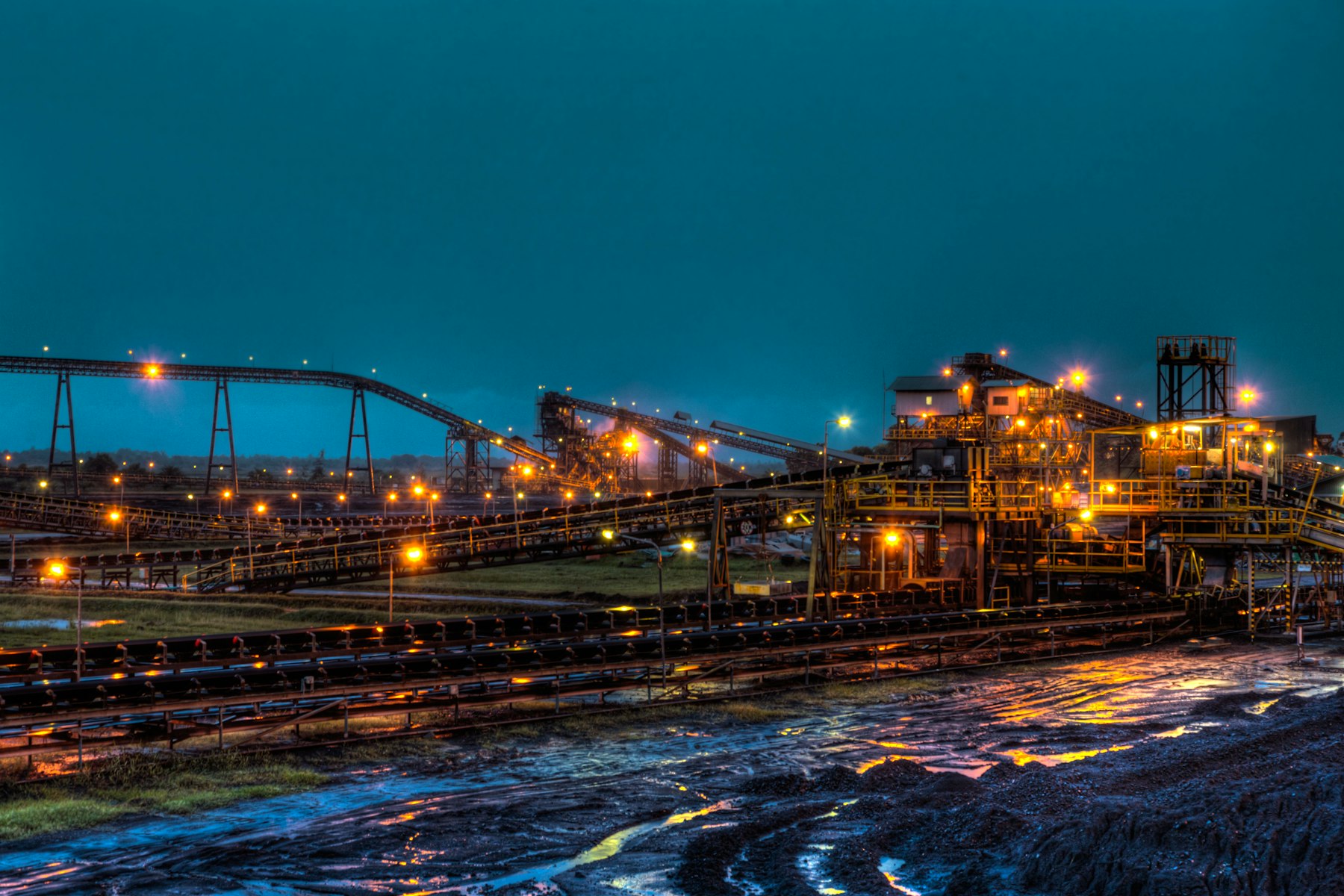 A mine processing plant with conveyors and lights at dusk.