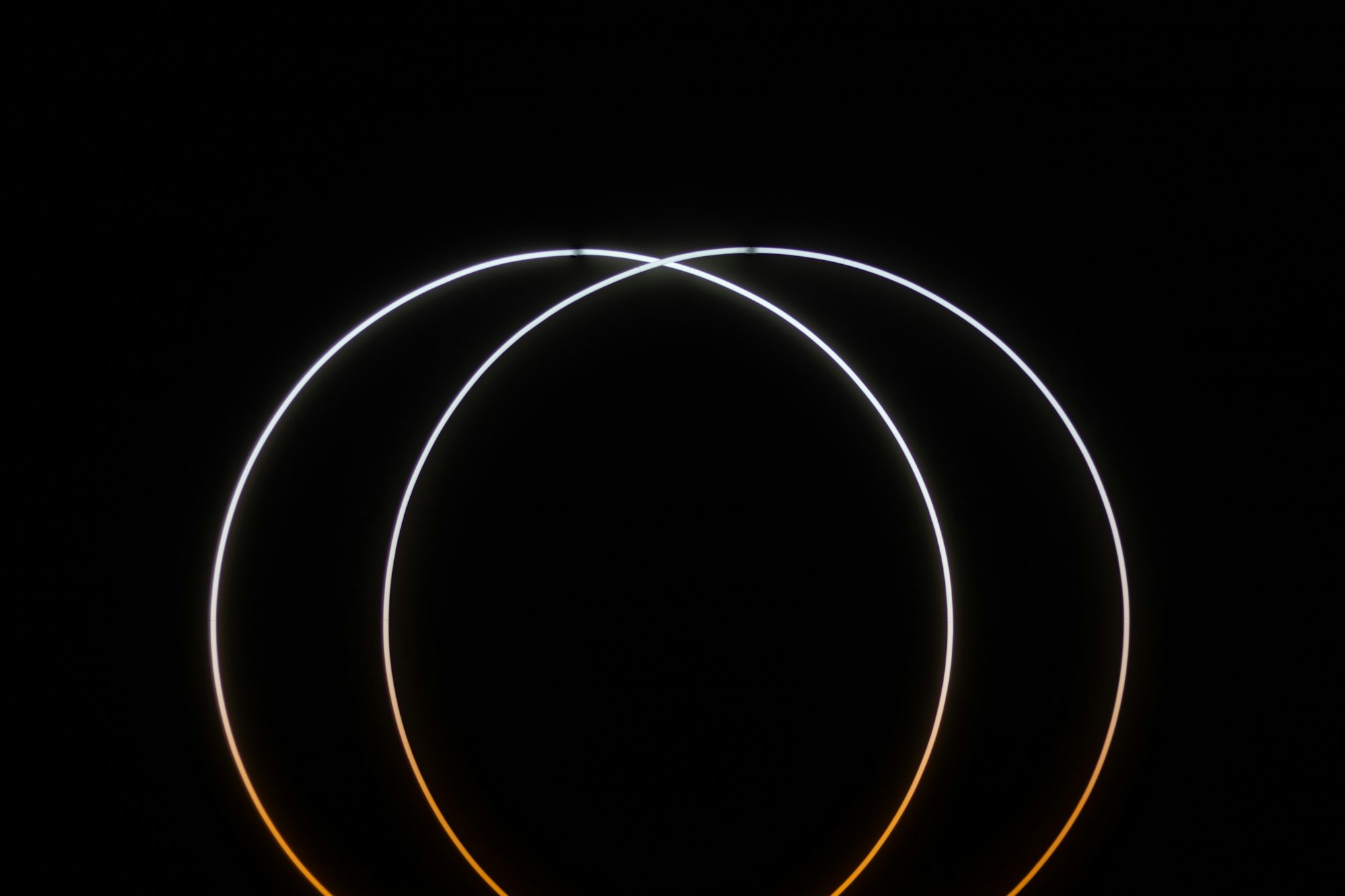Abstract pair of intersecting thin rings of light on a black background.