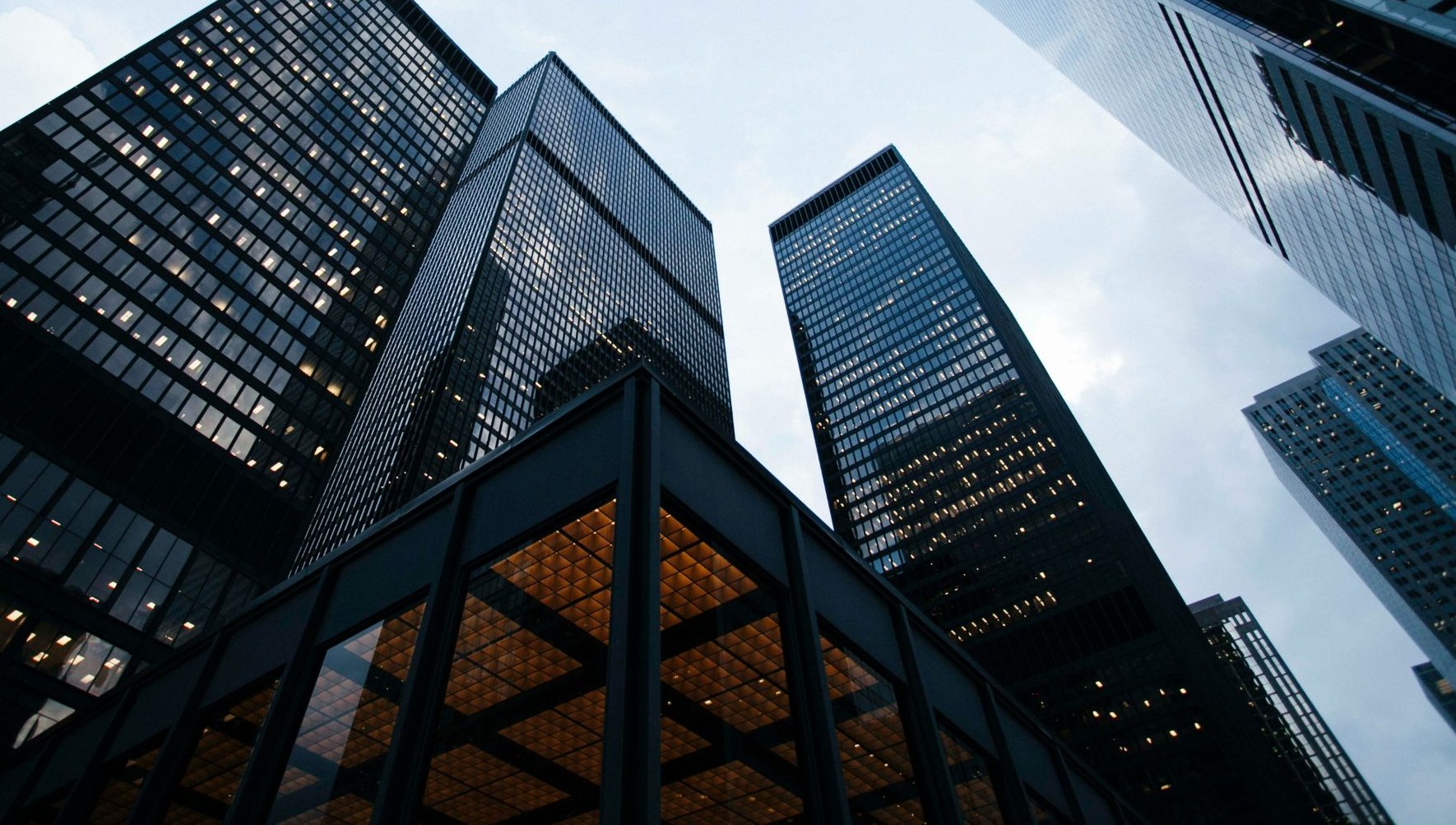 Glass office towers in a downtown business district at dusk, viewed from street level.