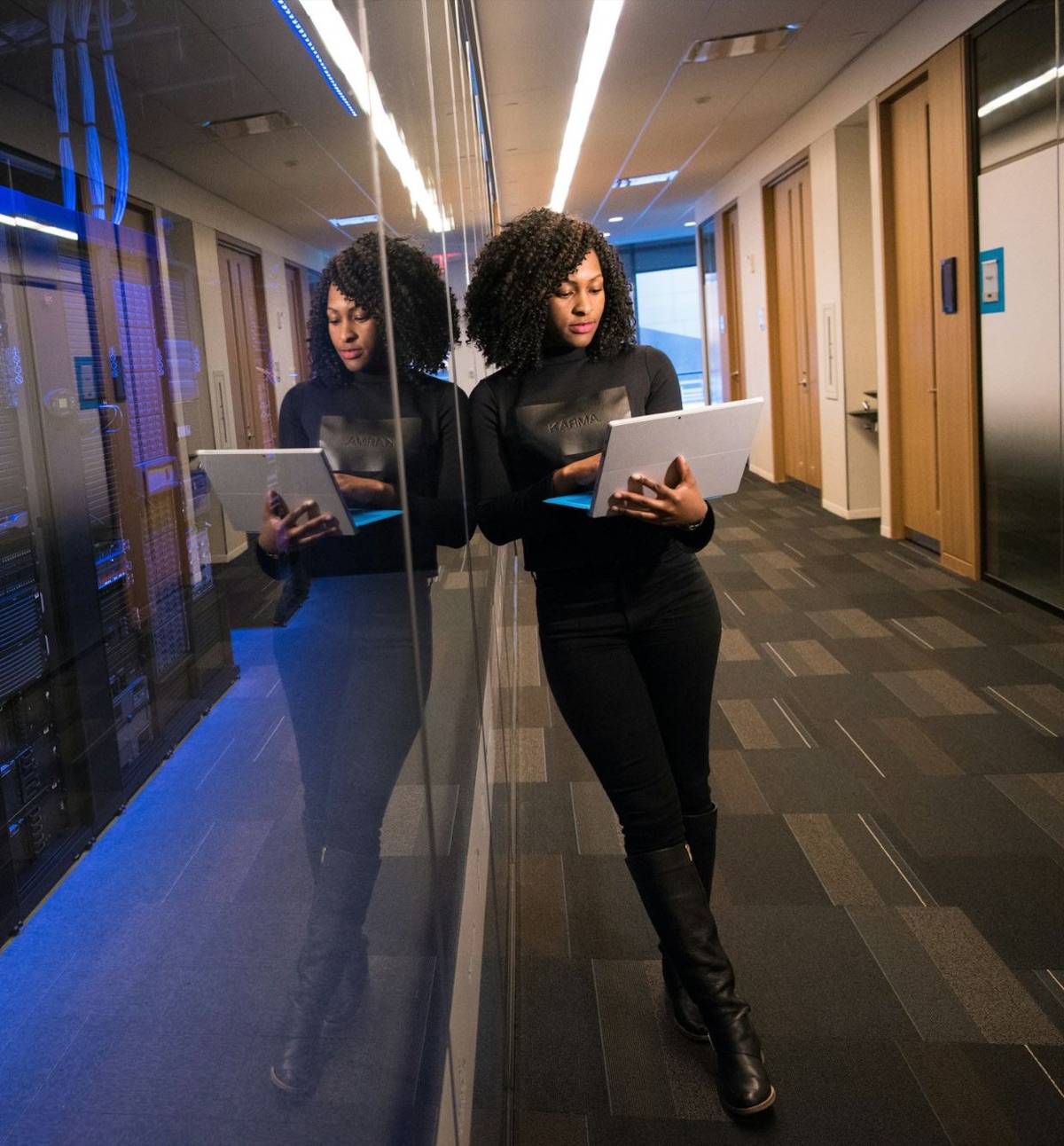 A technology professional reviewing a tablet beside a glass-walled server room.