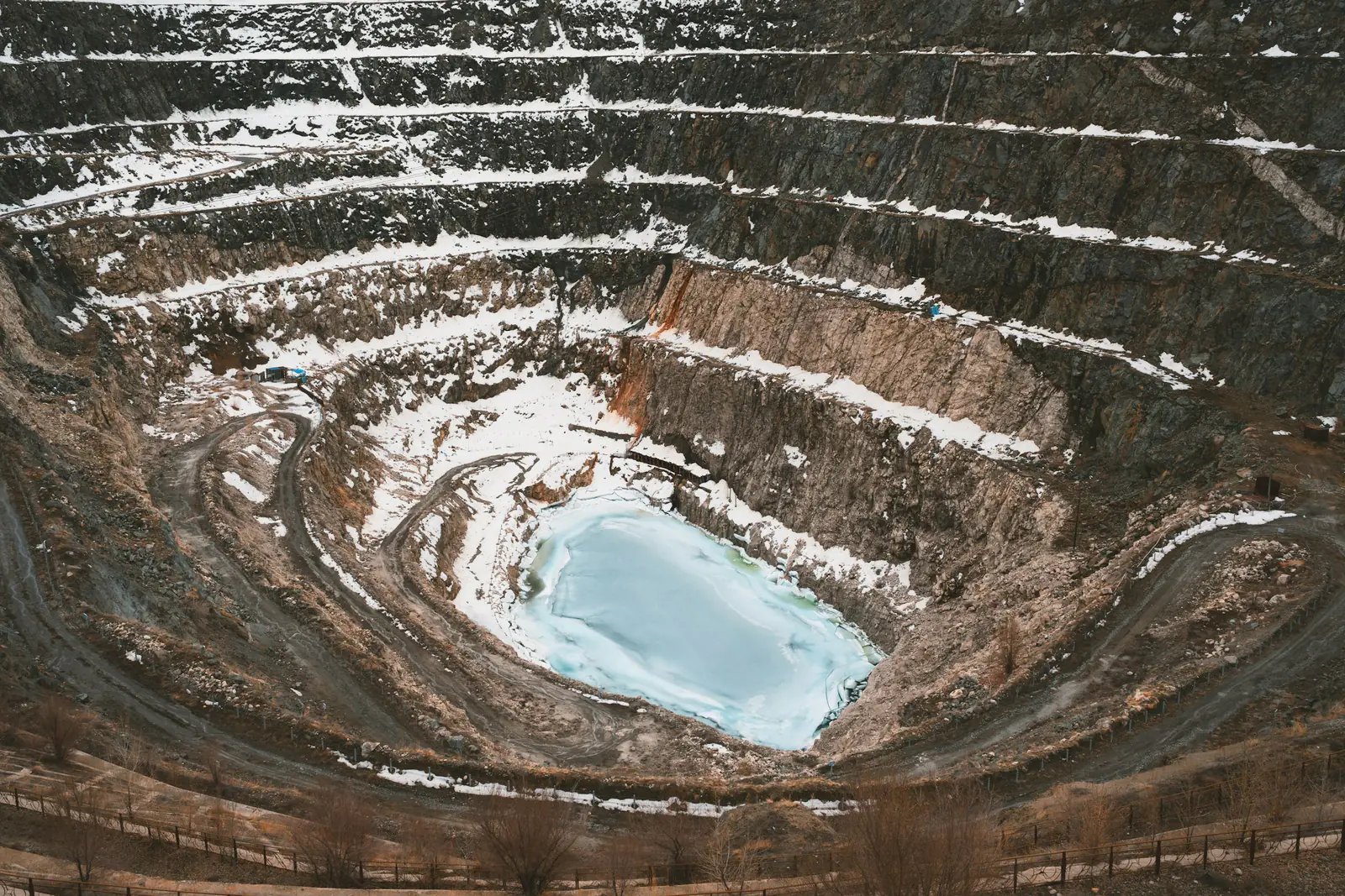 Aerial view of a terraced open-pit mine with snow on its benches and water at the base.