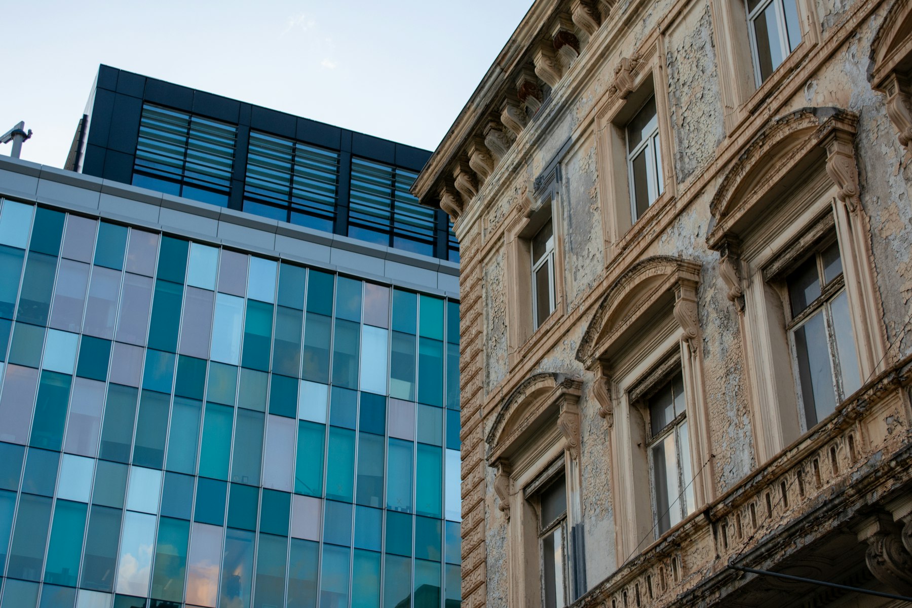 A modern glass building standing beside an older ornate facade.