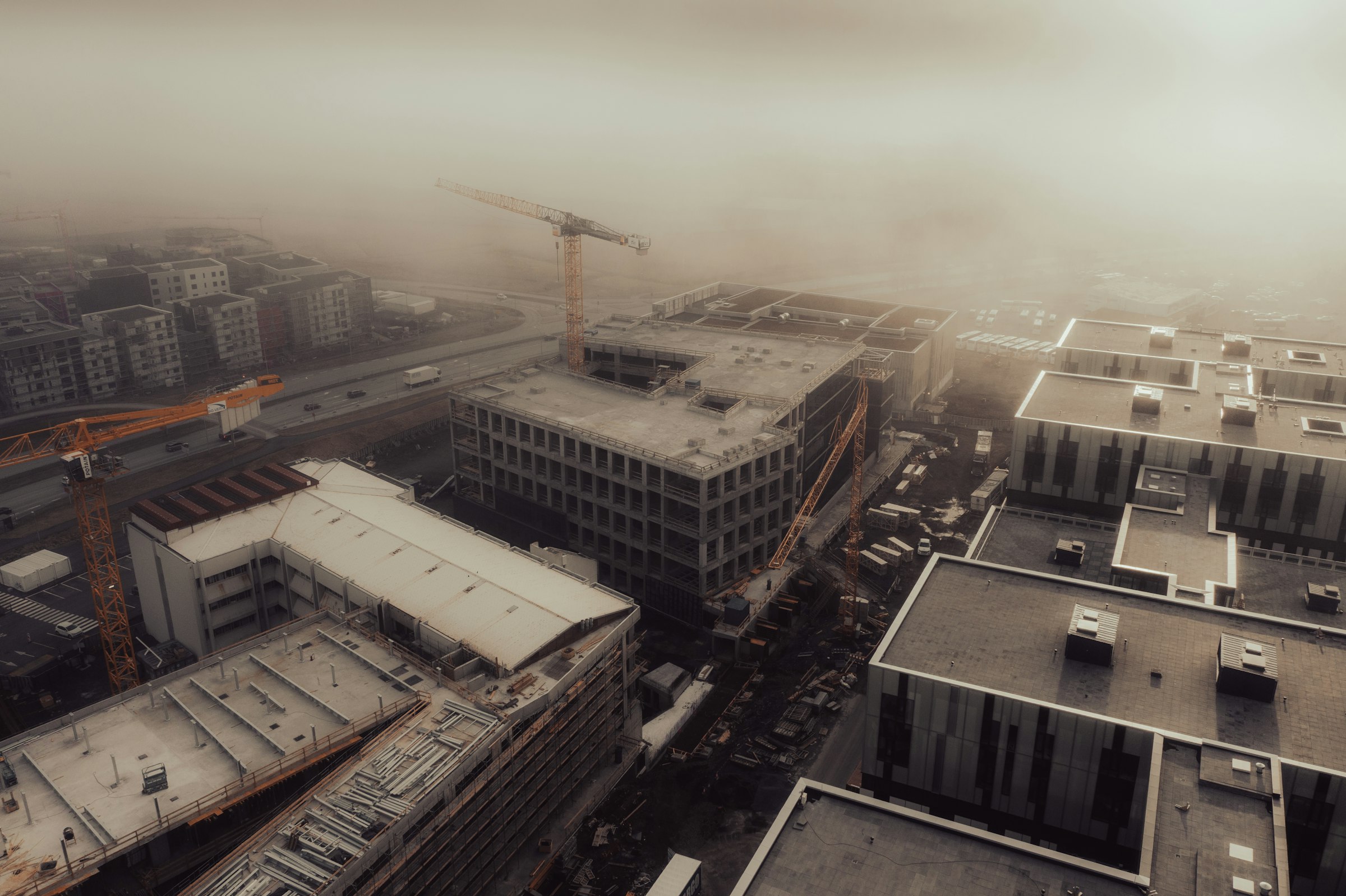 Tower cranes above buildings under construction on a foggy day.