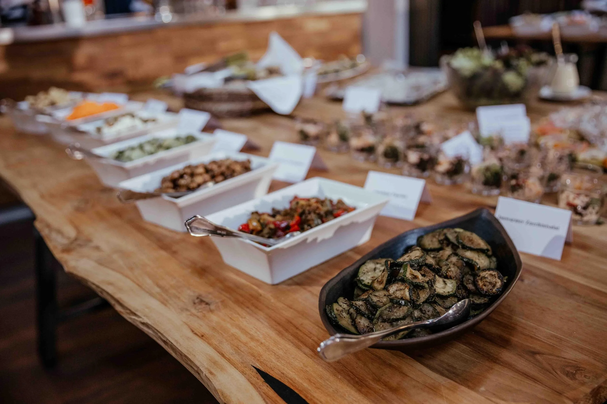 Buffet auf Holztischen mit gegrillter Zucchini und beschrifteten Tafelschildern