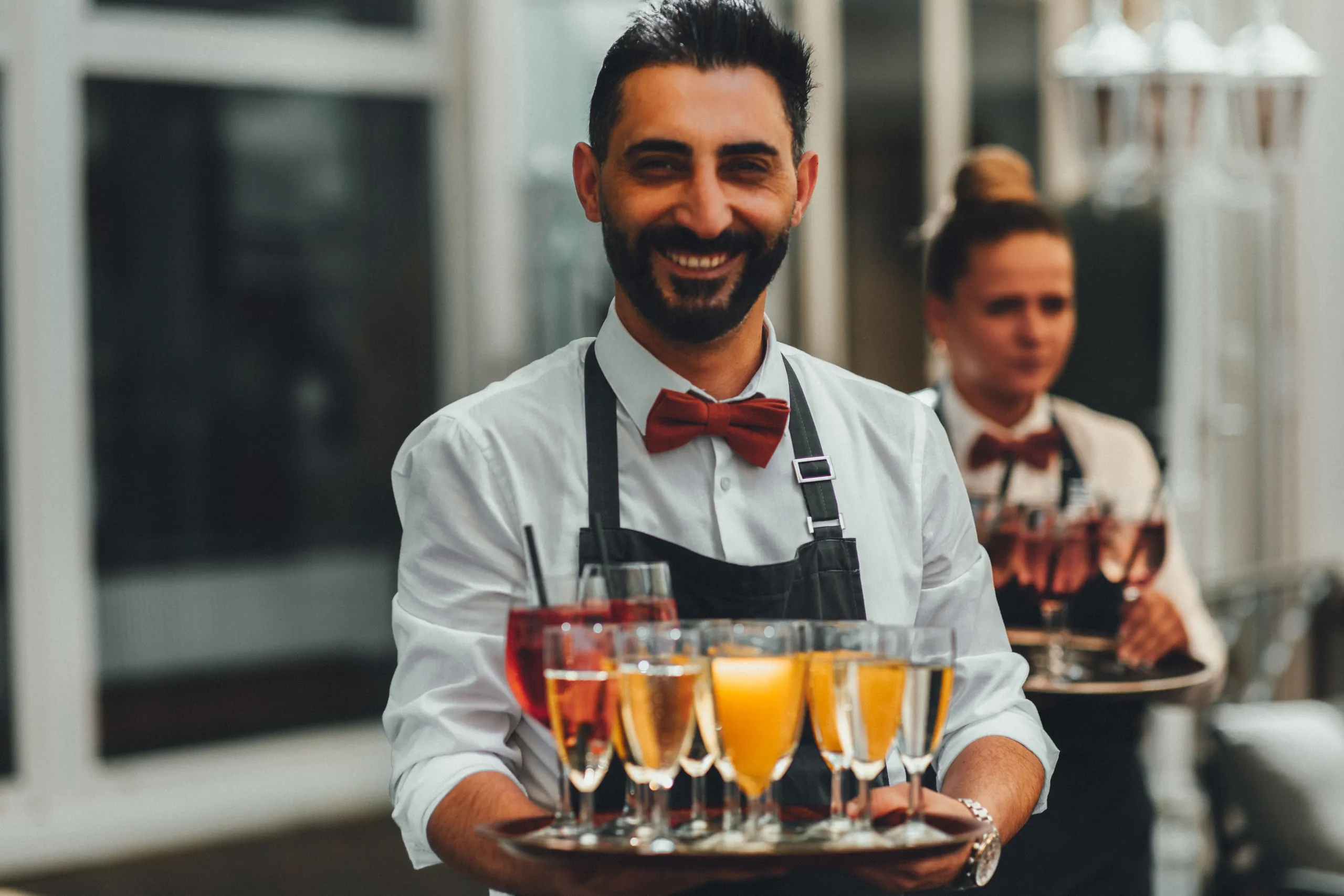 Kellner mit Fliege trägt ein Tablett mit Sekt und Orangensaft