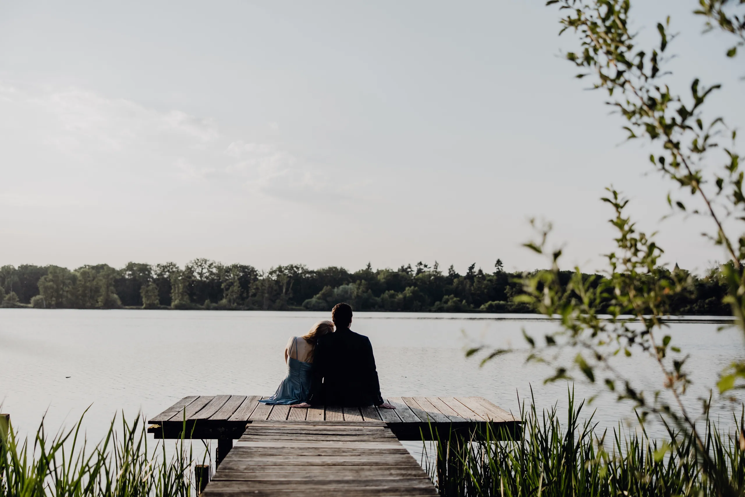 Brautpaar umarmt sich am Ende des Holzstegs, ringsum Schilf und der See