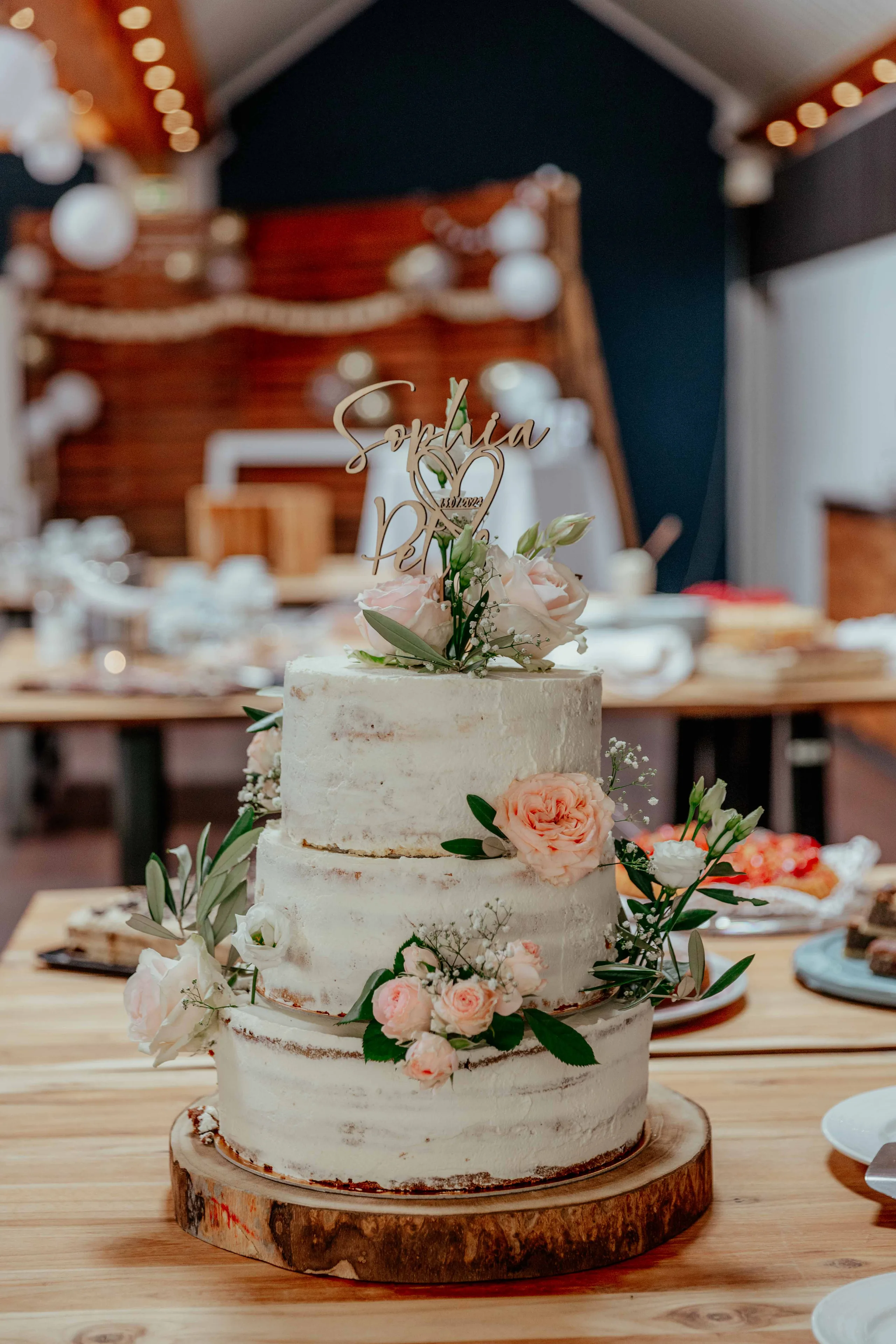 Dreistöckige Hochzeitstorte mit Rosen und Namensschild auf einer Holzscheibe