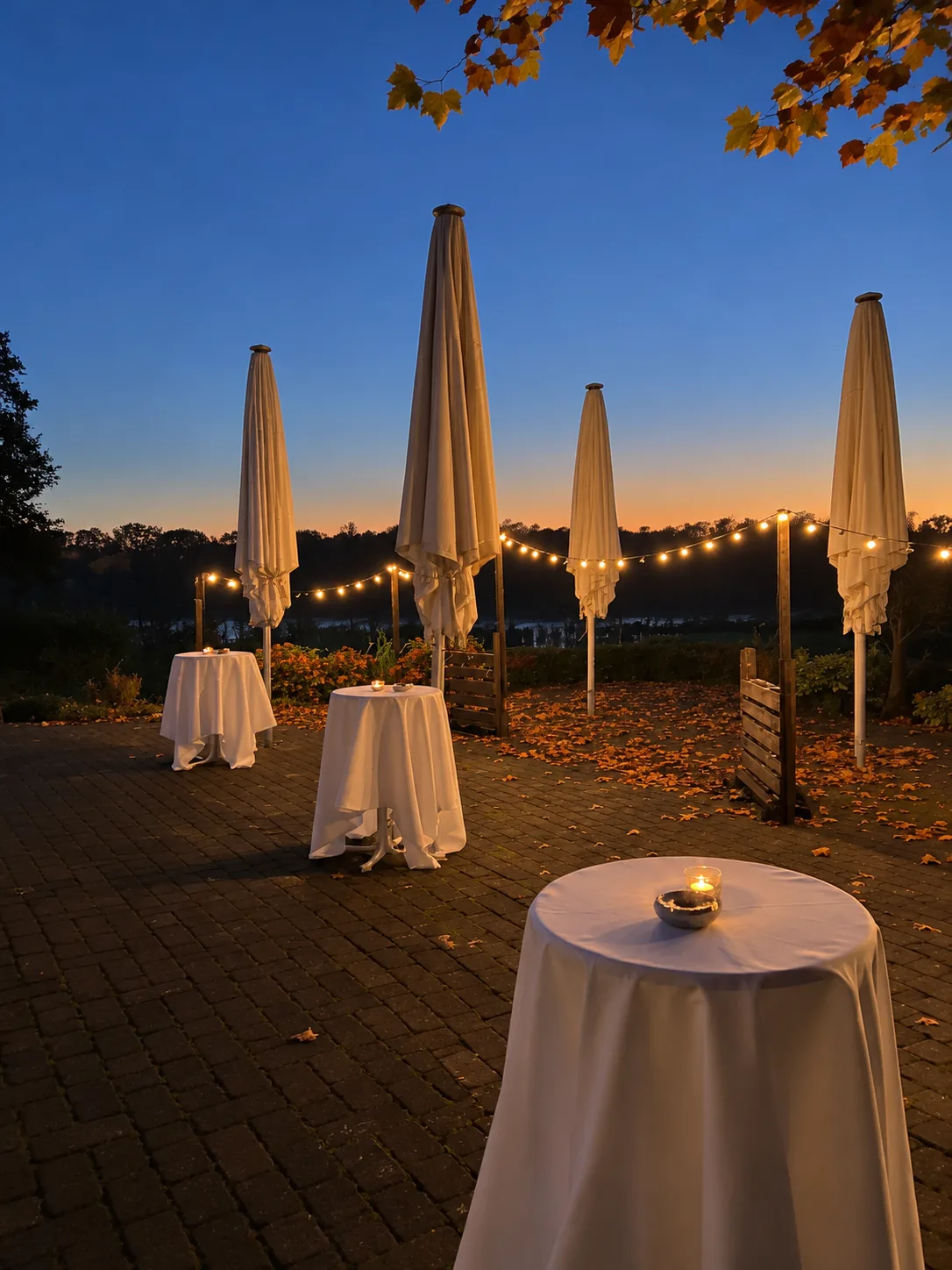 Stehtische auf der Seeterrasse in der Abenddämmerung, dahinter Lichterketten und der See