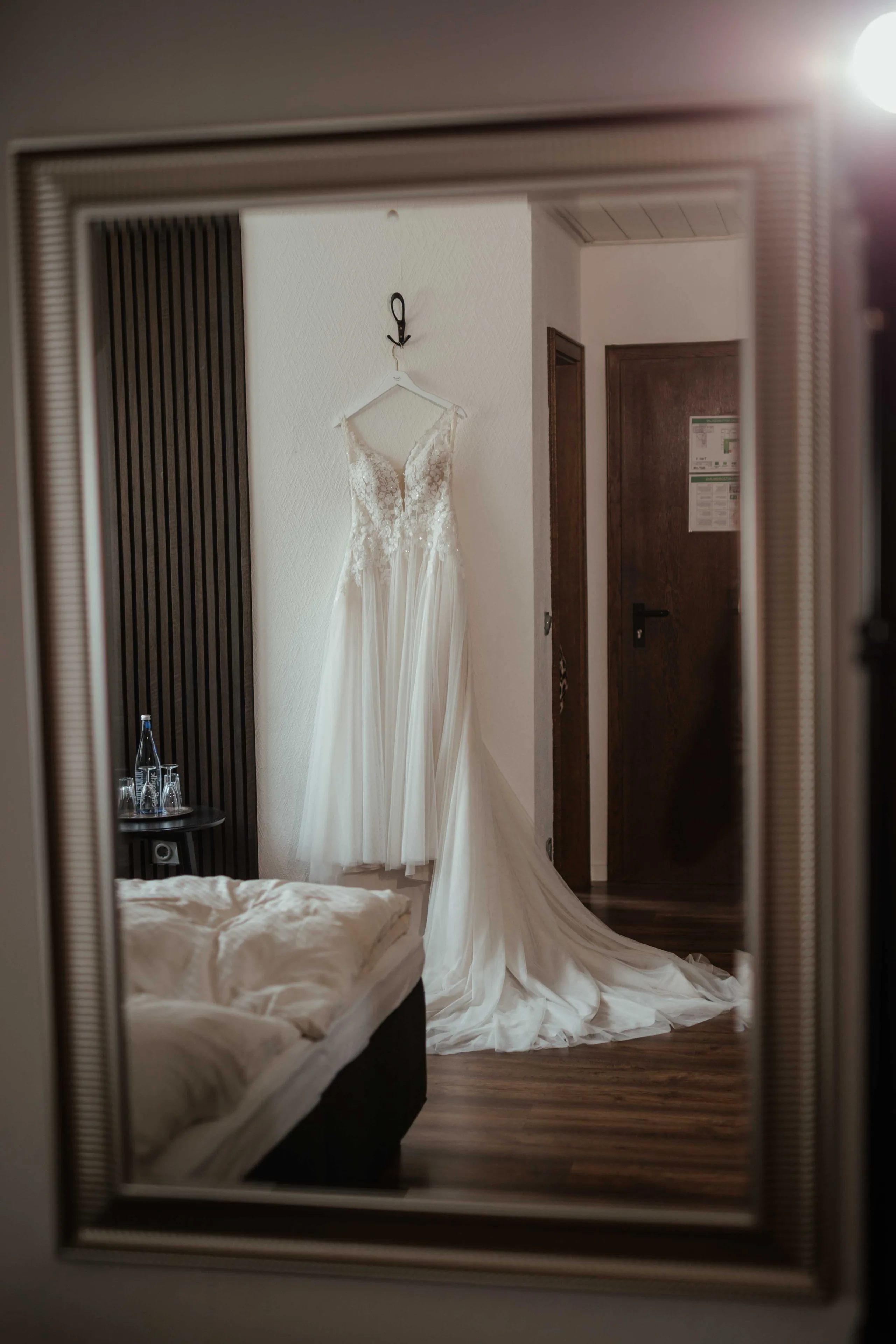 Brautkleid hängt im Zimmer, gespiegelt in einem großen Spiegel, davor das Bett
