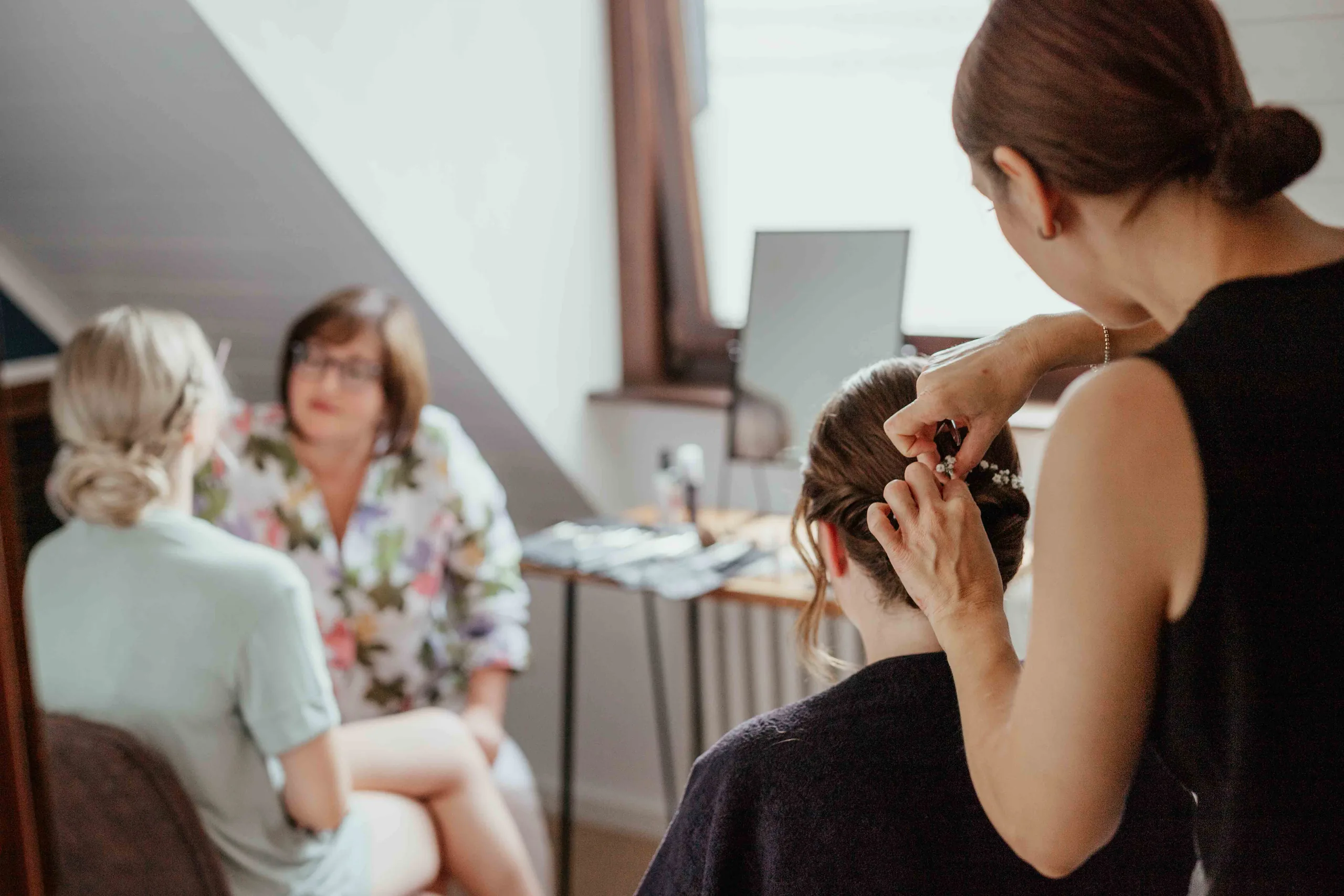 Braut wird unter der Dachschräge frisiert, im Hintergrund sitzen zwei Frauen