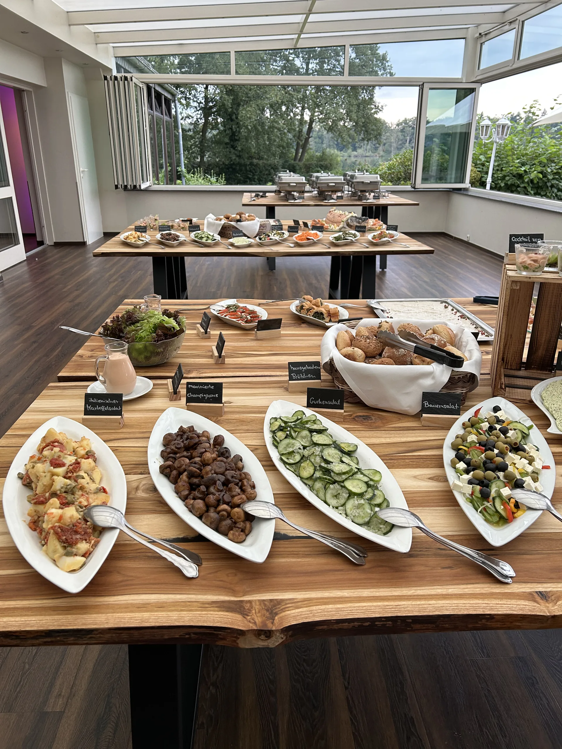 Buffet im Wintergarten mit Salaten, Antipasti und Brötchen, dahinter die geöffneten Fenster