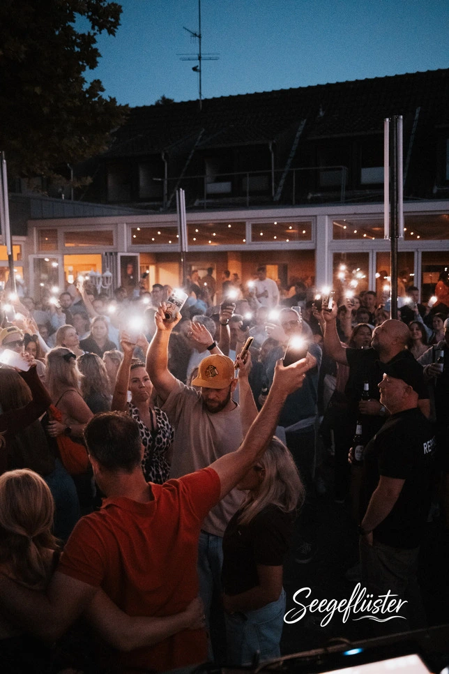 Gäste feiern am Abend vor dem Haus und halten Handylichter in die Höhe