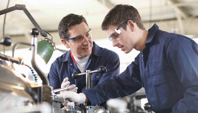 Two engineers in safety glasses working together at a machine in a workshop
