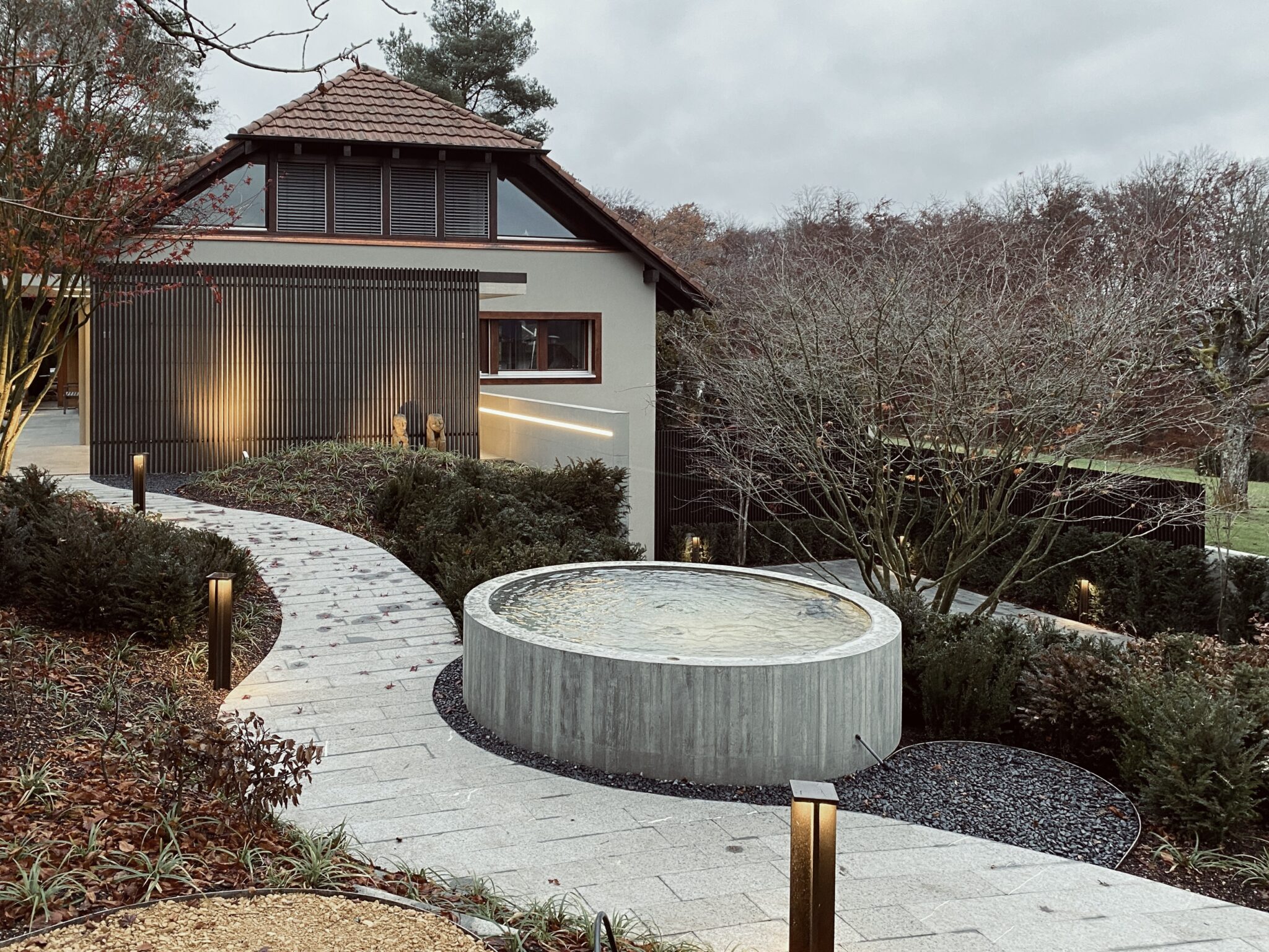 Umbau³ in Lupsingen: Garten mit Brunnen und Unterstand in der Dämmerung