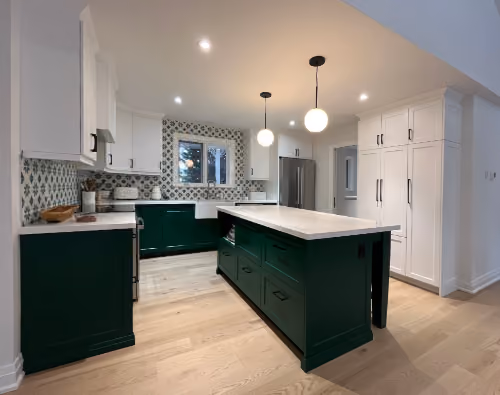 Modern kitchen with white upper cabinets, dark green lower cabinets and island with white countertop, patterned tile backsplash, stainless steel refrigerator, and light wood flooring.