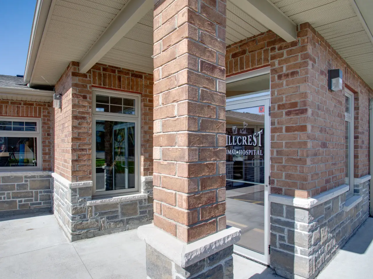 Entrance of a brick and stone building with a glass door displaying the sign 'Hillcrest Animal Hospital'.