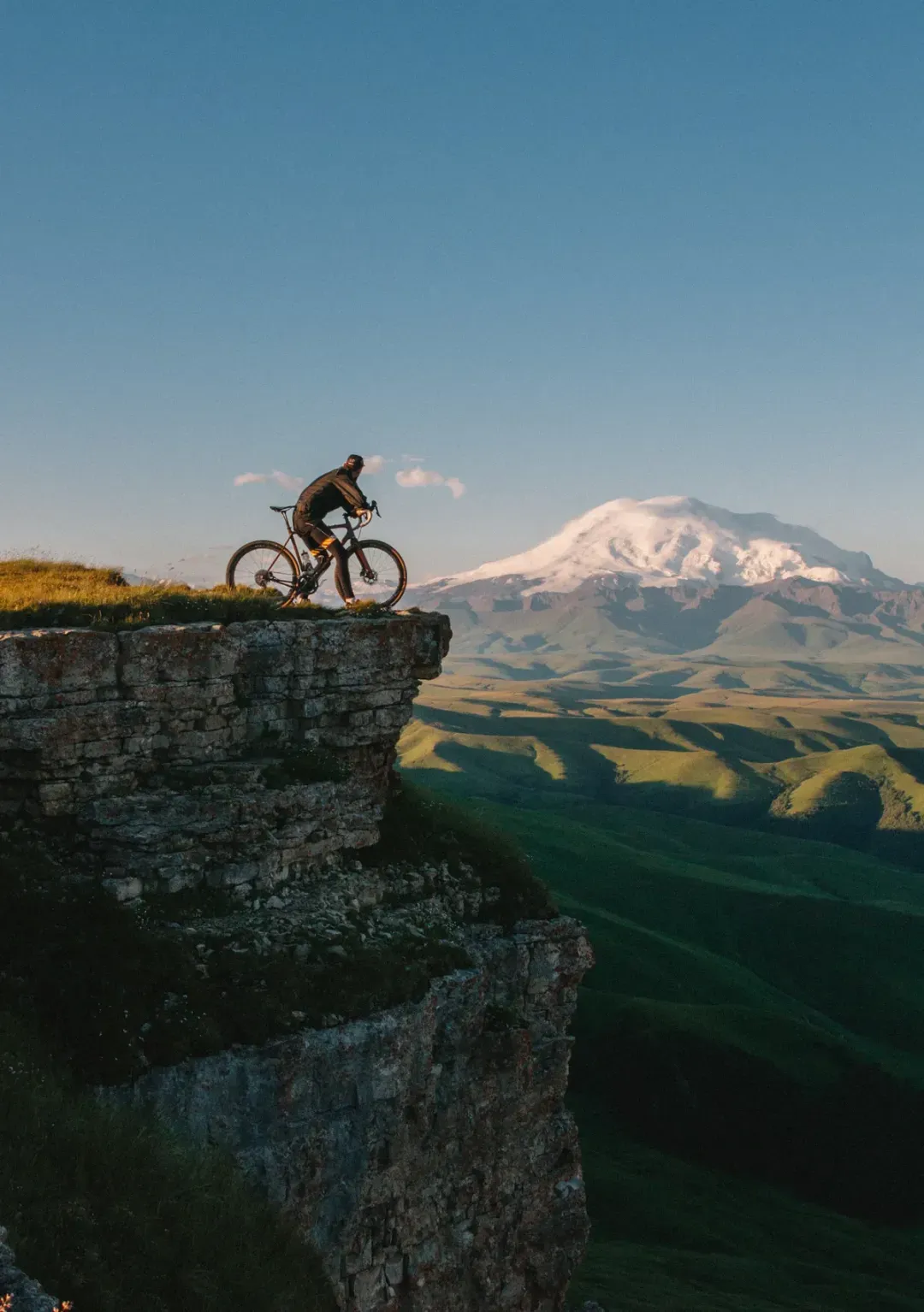 Mountainbiker an einer Felskante vor verschneitem Berg – Cleverbikes