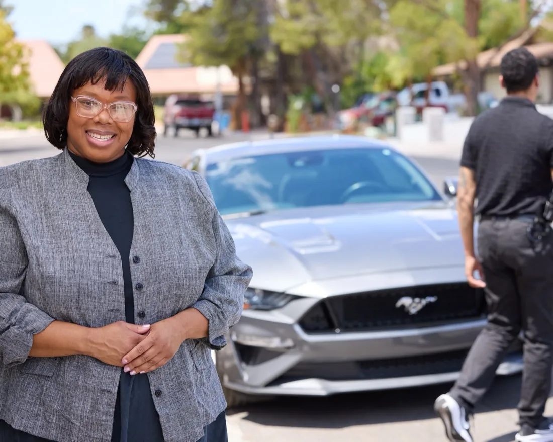 Kamilah Bywaters in a gray jacket standing in front of a silver car