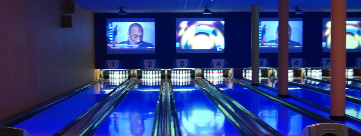 Bowling lanes lit with blue light and large TV screens above the pins