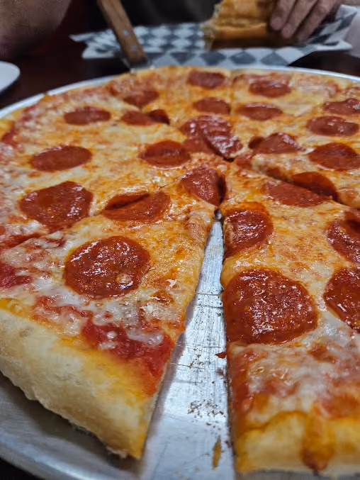 Close-up of a pepperoni pizza on a metal tray with one slice slightly pulled out, showing melted cheese and tomato sauce.