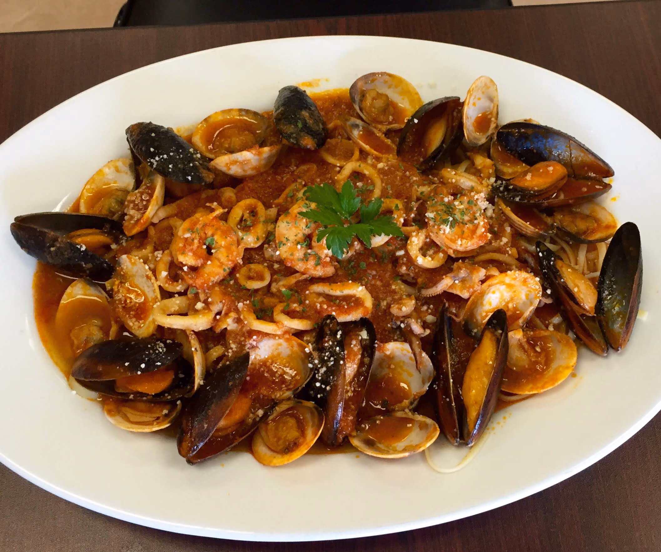 Plate of seafood pasta with shrimp, mussels, clams, and squid rings in a red tomato sauce, garnished with parsley on top.
