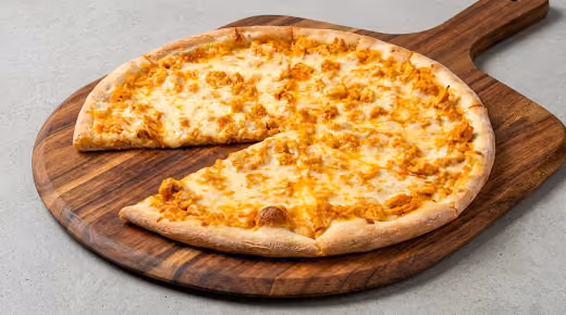 Buffalo chicken pizza with chunks of chicken and melted cheese on a wooden pizza board, with one slice slightly separated.