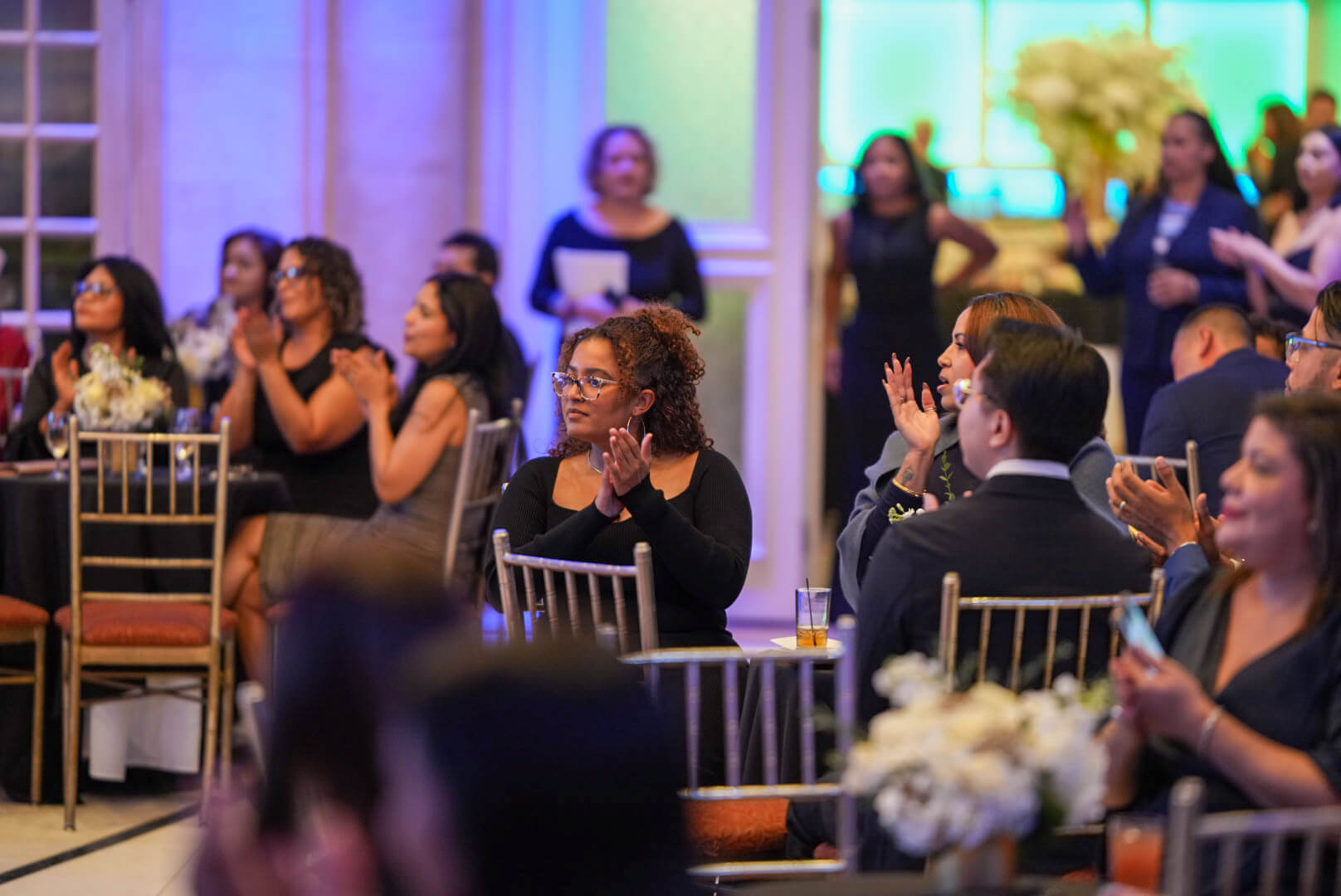 Guests seated at dinner tables applaud during the program.