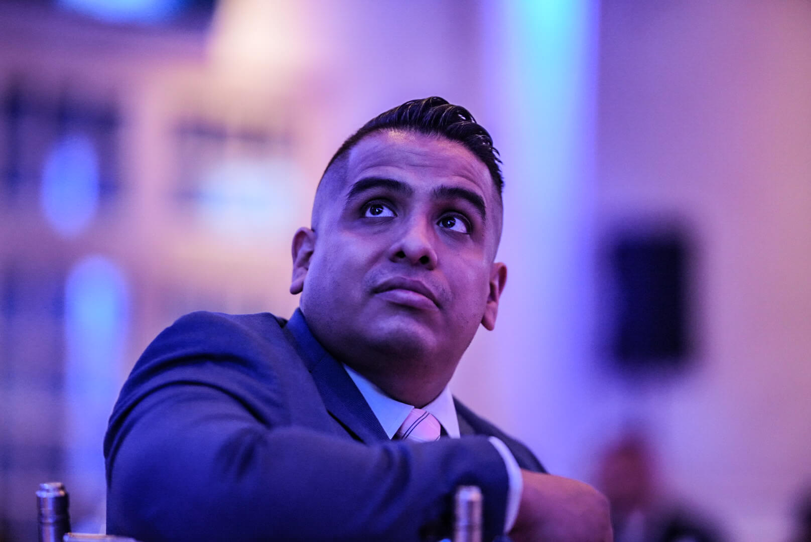 A guest in a navy suit looks up toward the stage under purple lighting.
