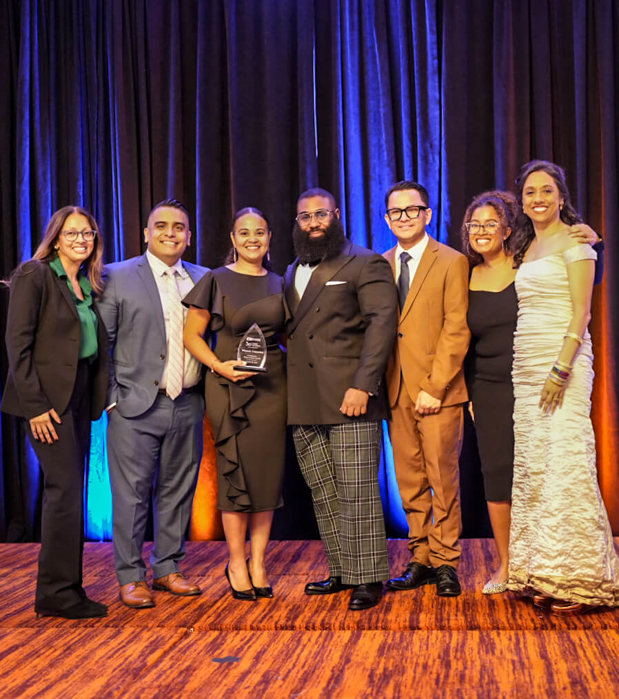 Honorees and presenters line up for a group photo on stage, one holding an award.