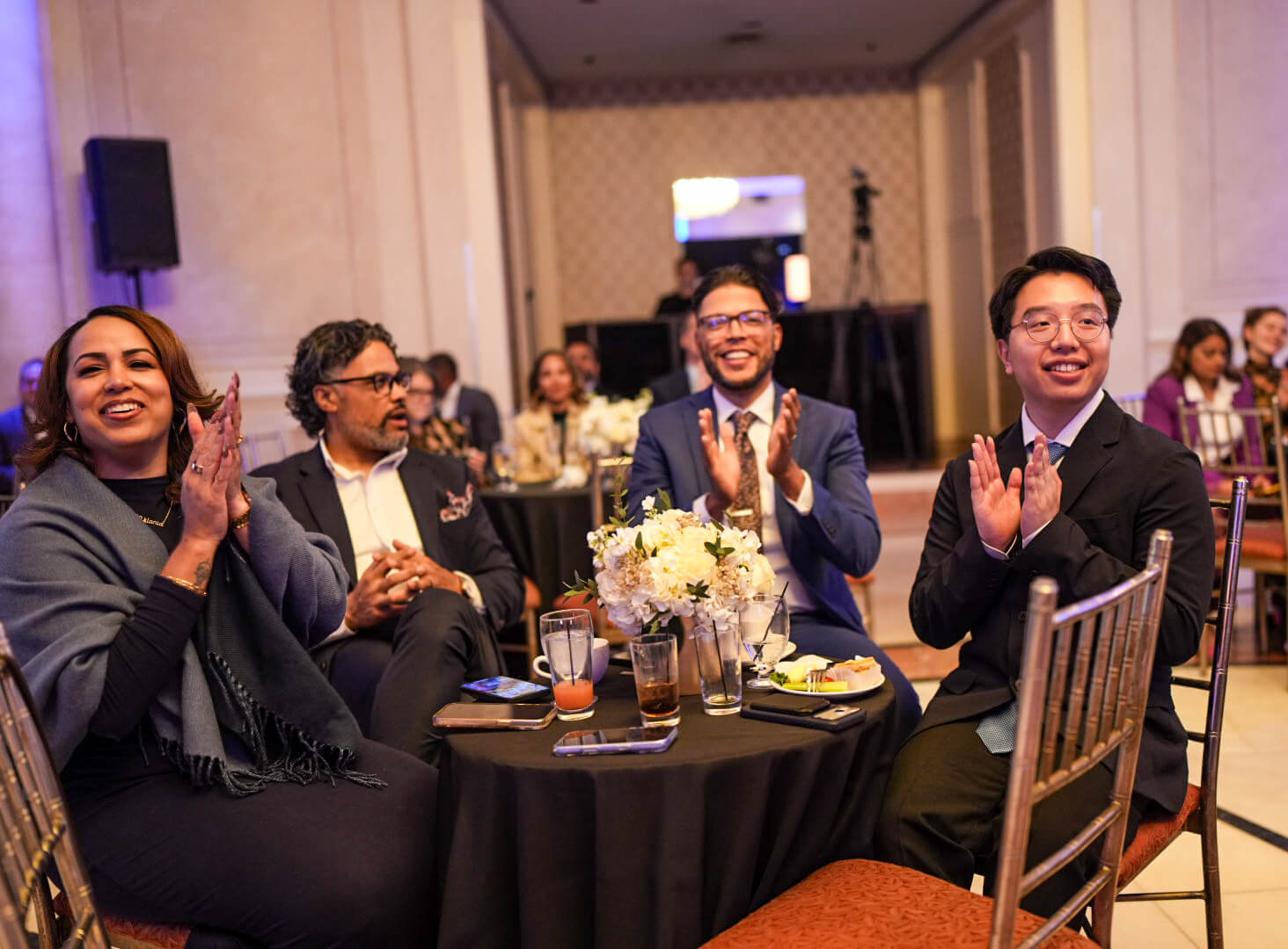 Guests at a dinner table smile and applaud.