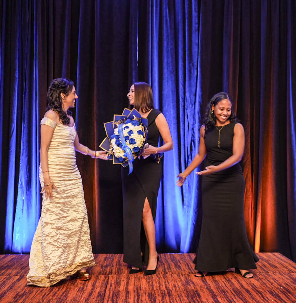 An honoree is presented with a bouquet of blue and white flowers on stage.