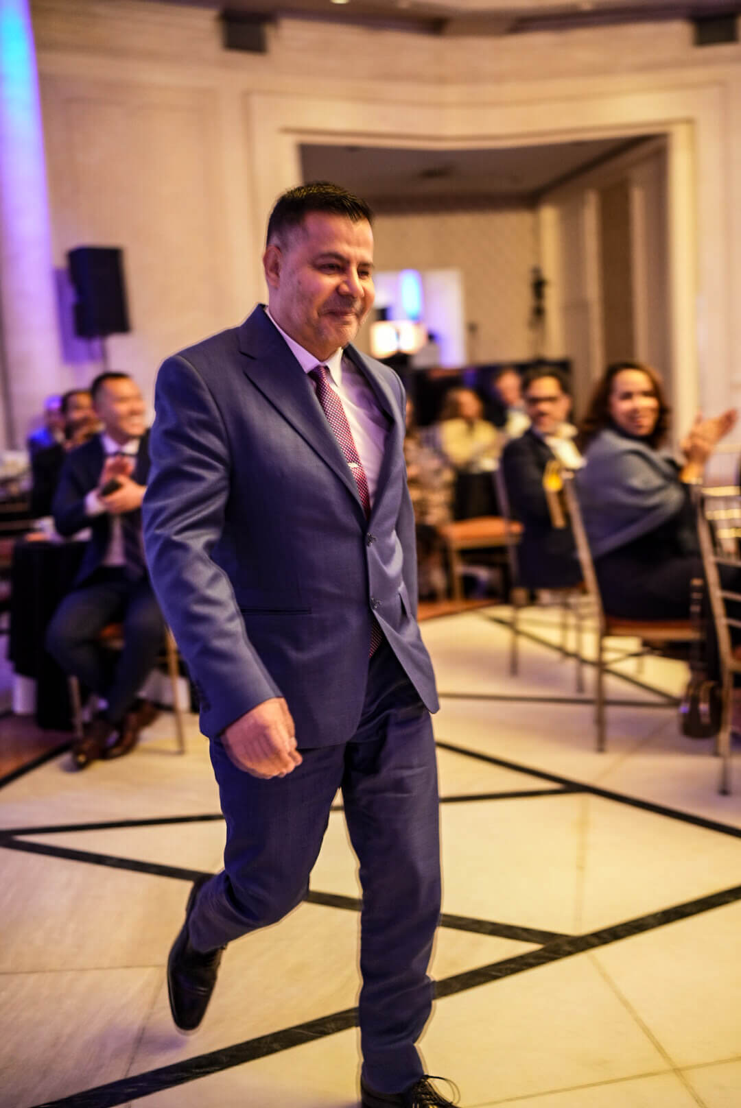A guest in a navy suit smiles as he walks across the ballroom.