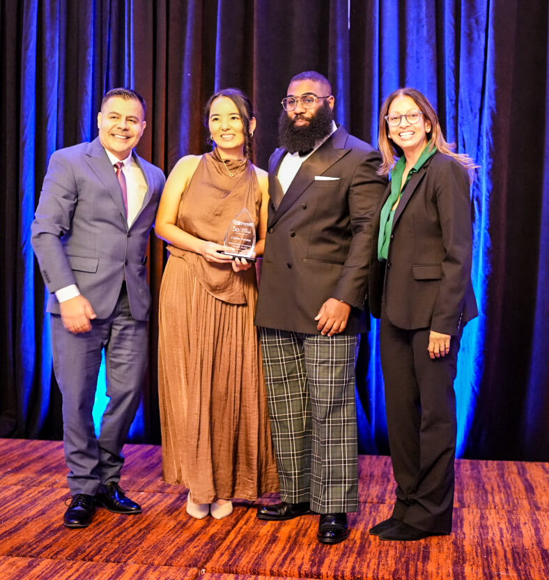 Four people pose on stage, one holding a crystal award.