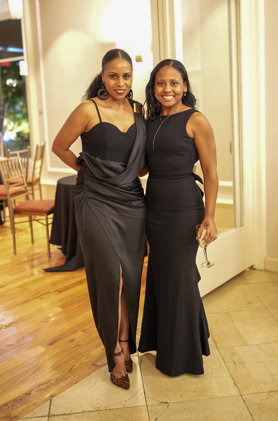 Two women in black evening dresses pose together in the reception room.
