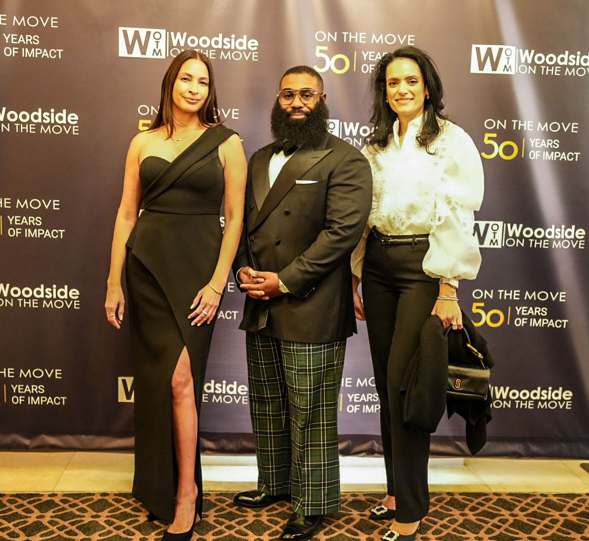 Three guests in formal wear pose in front of the 50 Years of Impact backdrop.